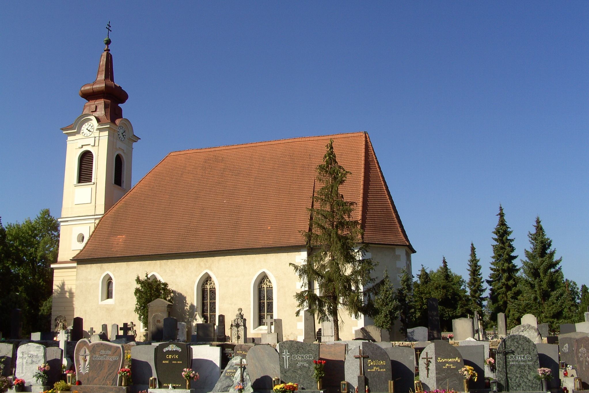 Egy templom külső nézete, előtérben egy temetővel és kék éggel.