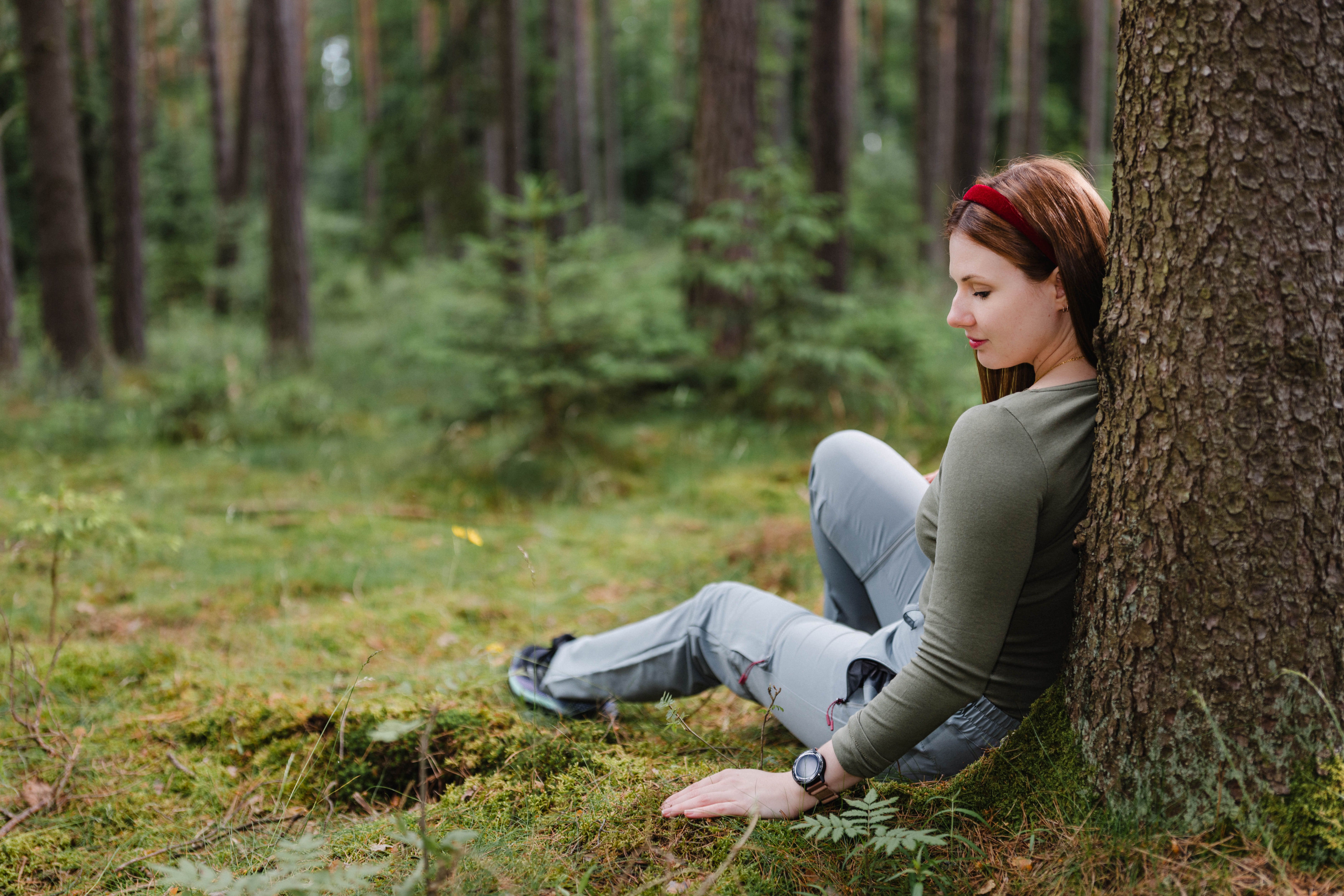 Nő egy fának támaszkodva az erdőben.