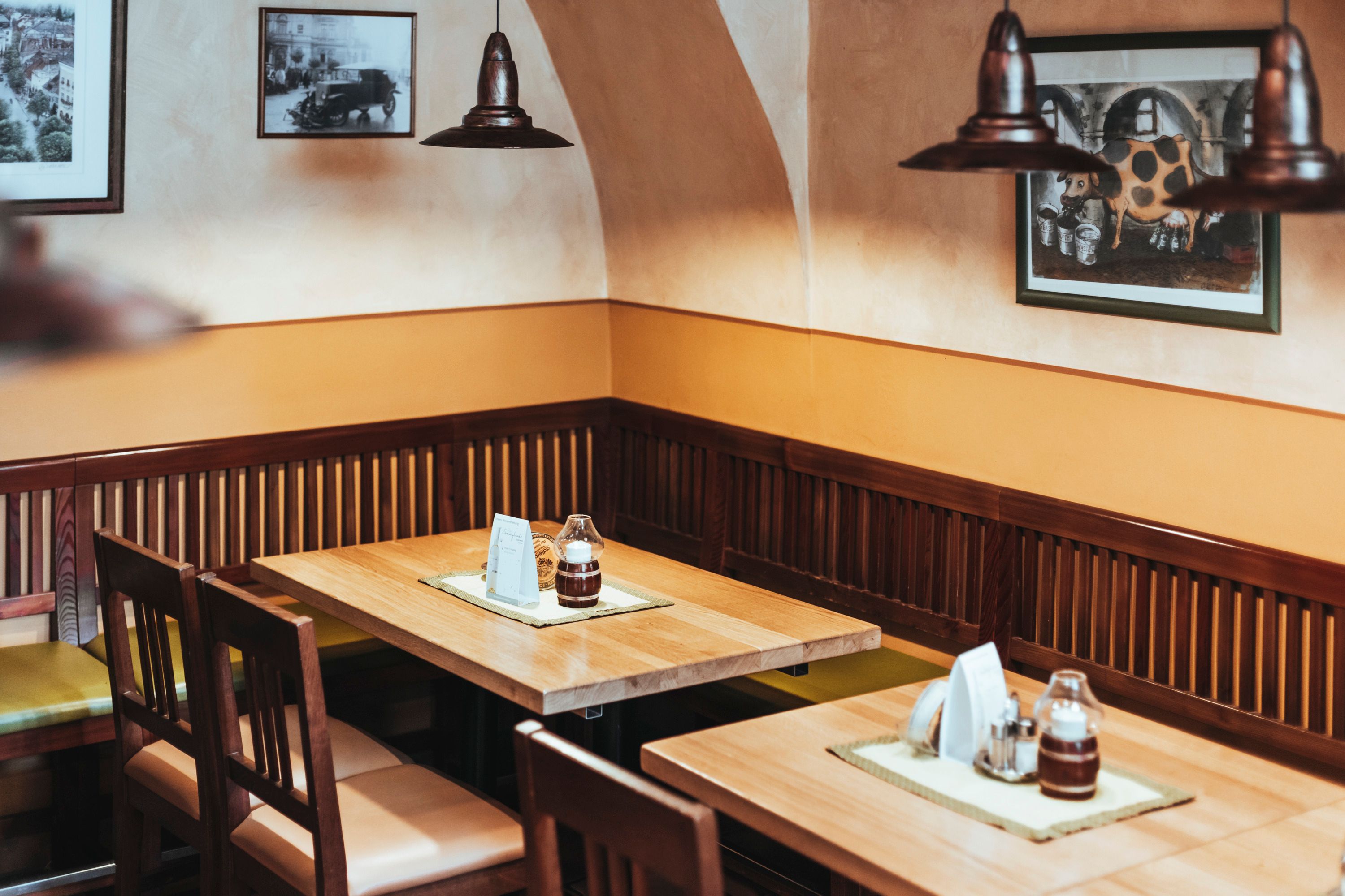 Hangulatos ülőhely az étteremben, fa asztalokkal és székekkel, a falon képekkel díszített.