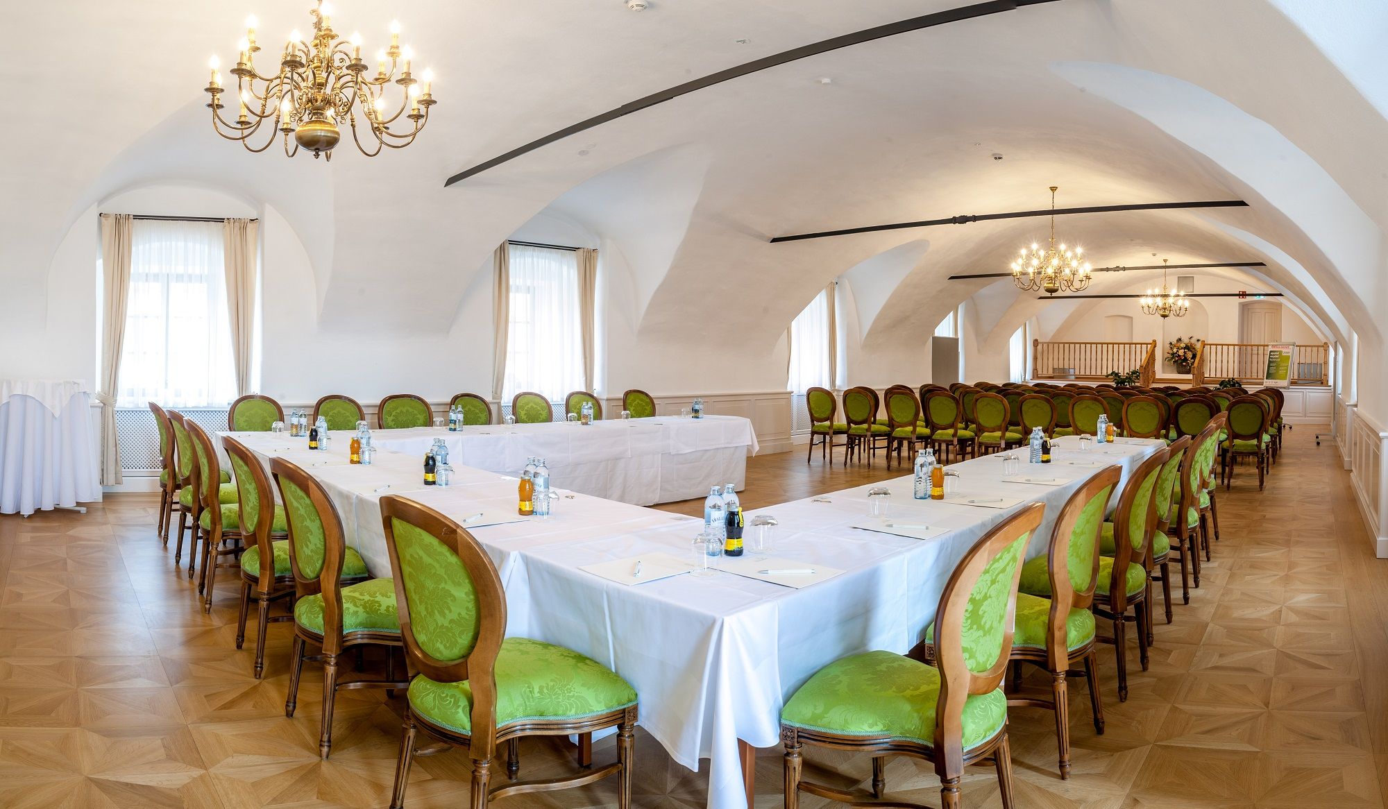 Elegáns konferenciaterem a thalheimi kastélyban, zöld székekkel és csillárokkal.