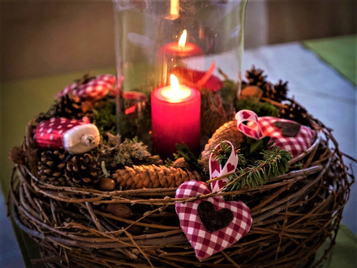 Adventi koszorú égő piros gyertyával, fenyőtobozokkal és piros-fehér kockás szövetszívekkel.