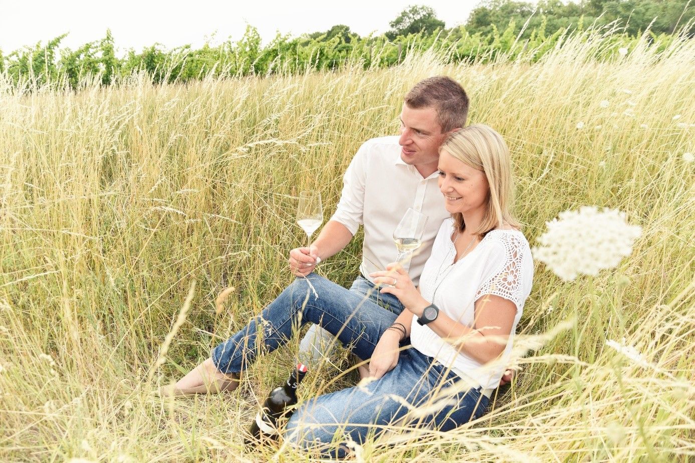 Egy pár ül a magas fűben és bort iszik.