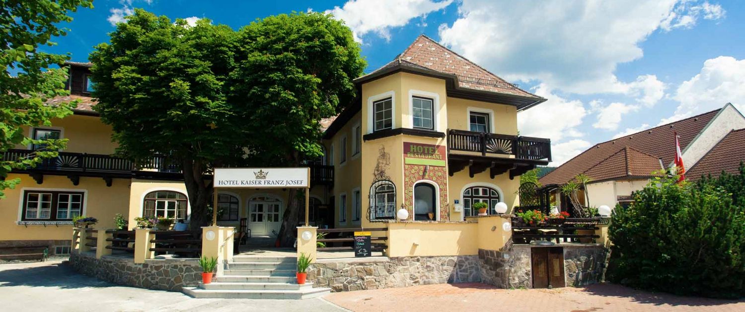 A Hotel Kaiser Franz Josef bejárata sárga homlokzattal és erkéllyel.