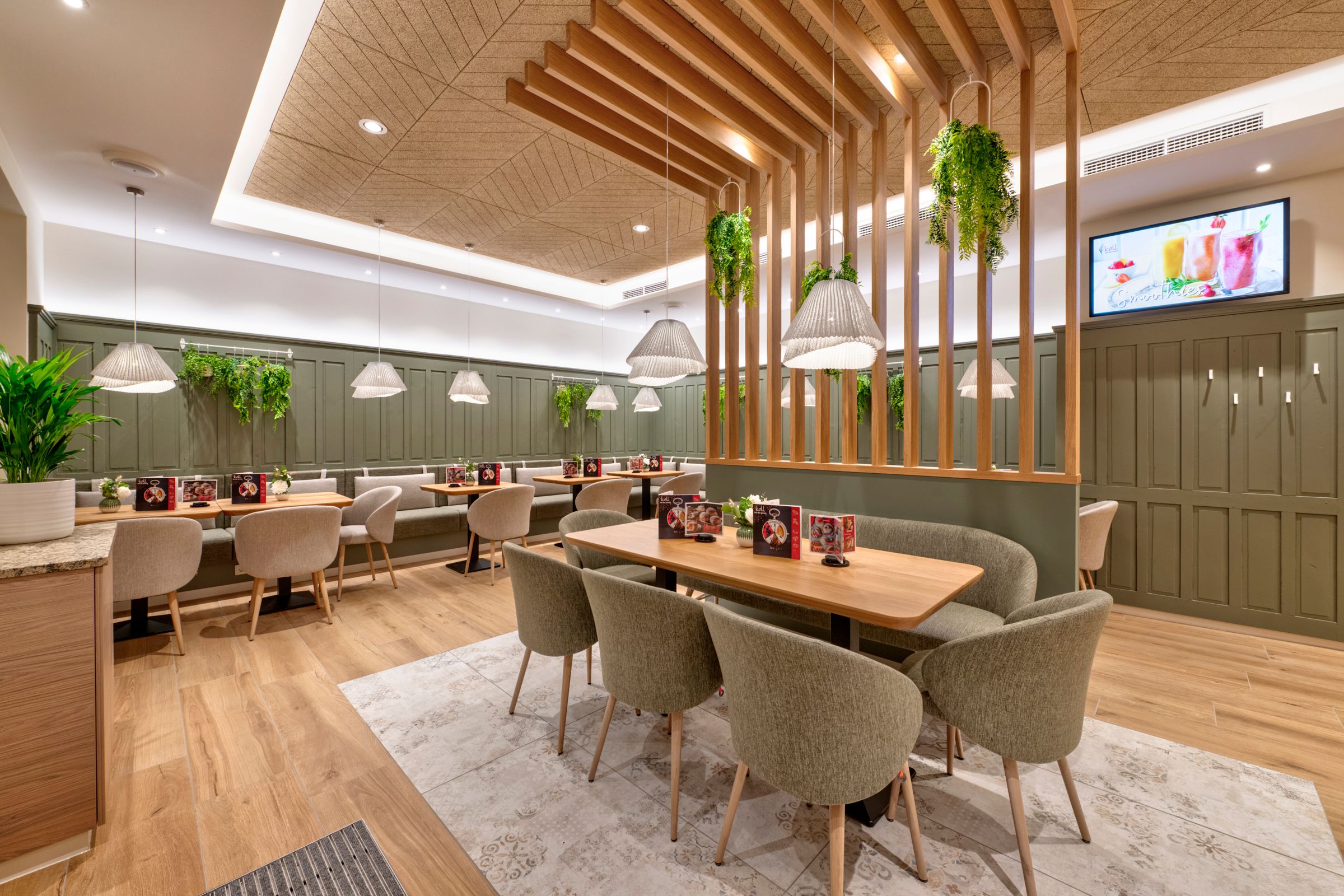 A modern kávézó belső nézete faasztalokkal, kárpitozott székekkel és lógó növényekkel.