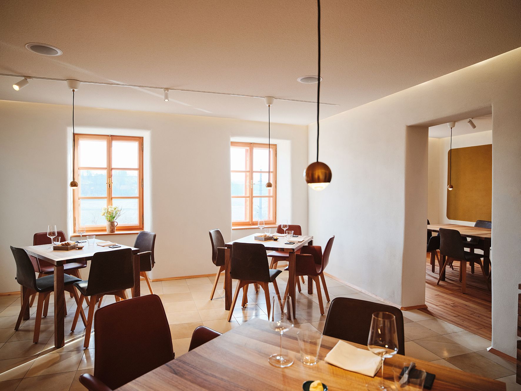 Modern étkező, fa asztalokkal, borospoharakkal és nagy ablakokkal, minimalista kialakításban.