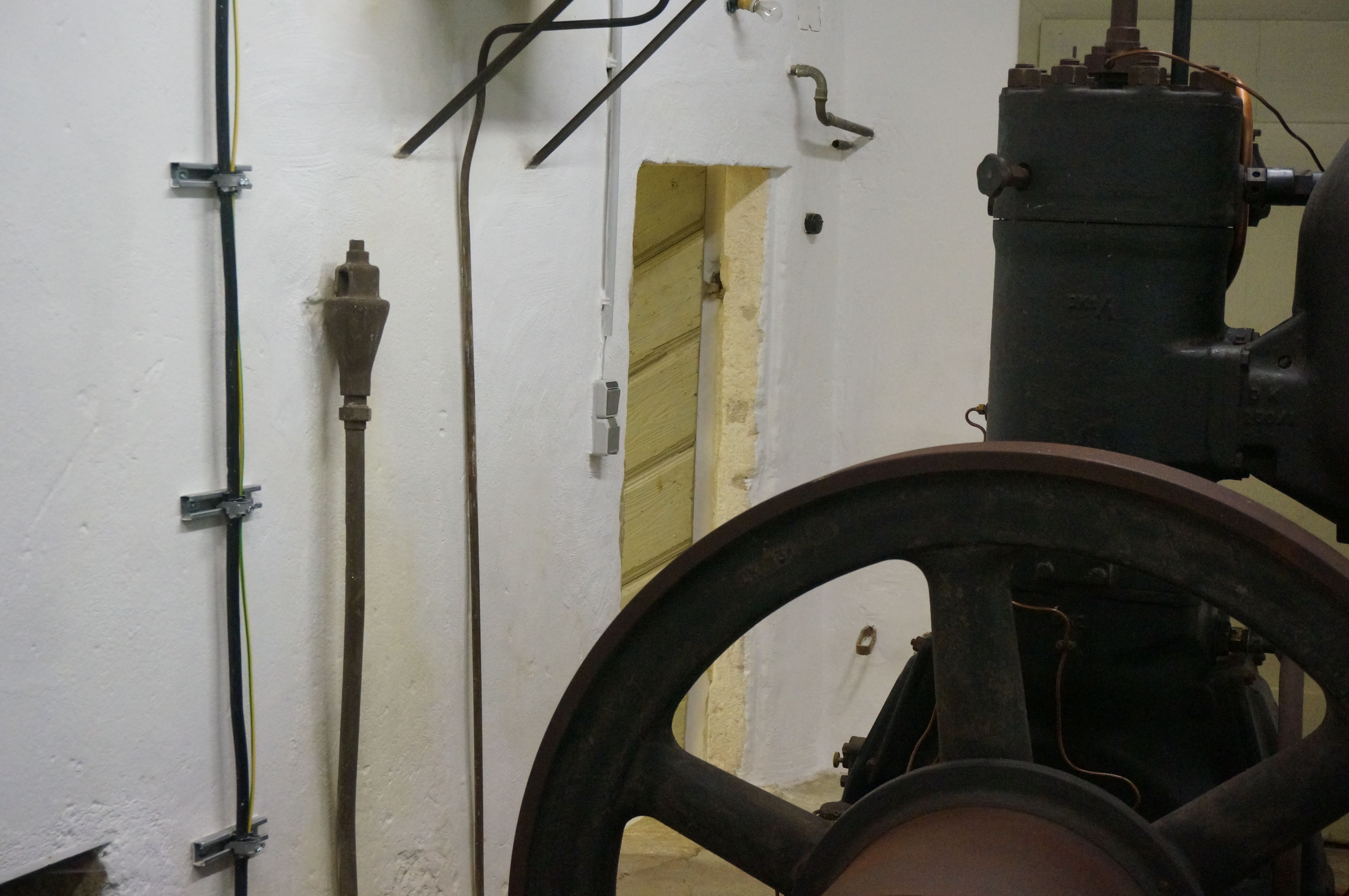 Régi motor egy fehér falakkal és kábelekkel teli szobában.