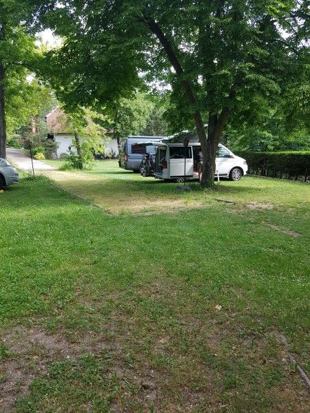 Két lakóautó parkol a fák alatt egy zöld kempingben.