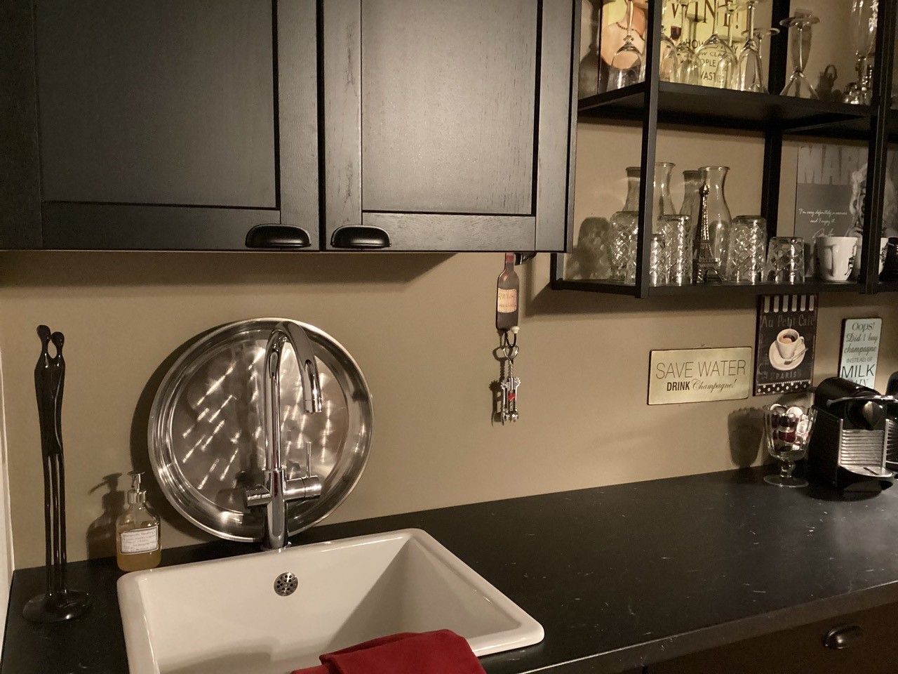 Modern konyhasarok mosogatóval, fekete szekrénnyel, polcokkal, poharakkal és kávéfőzővel.