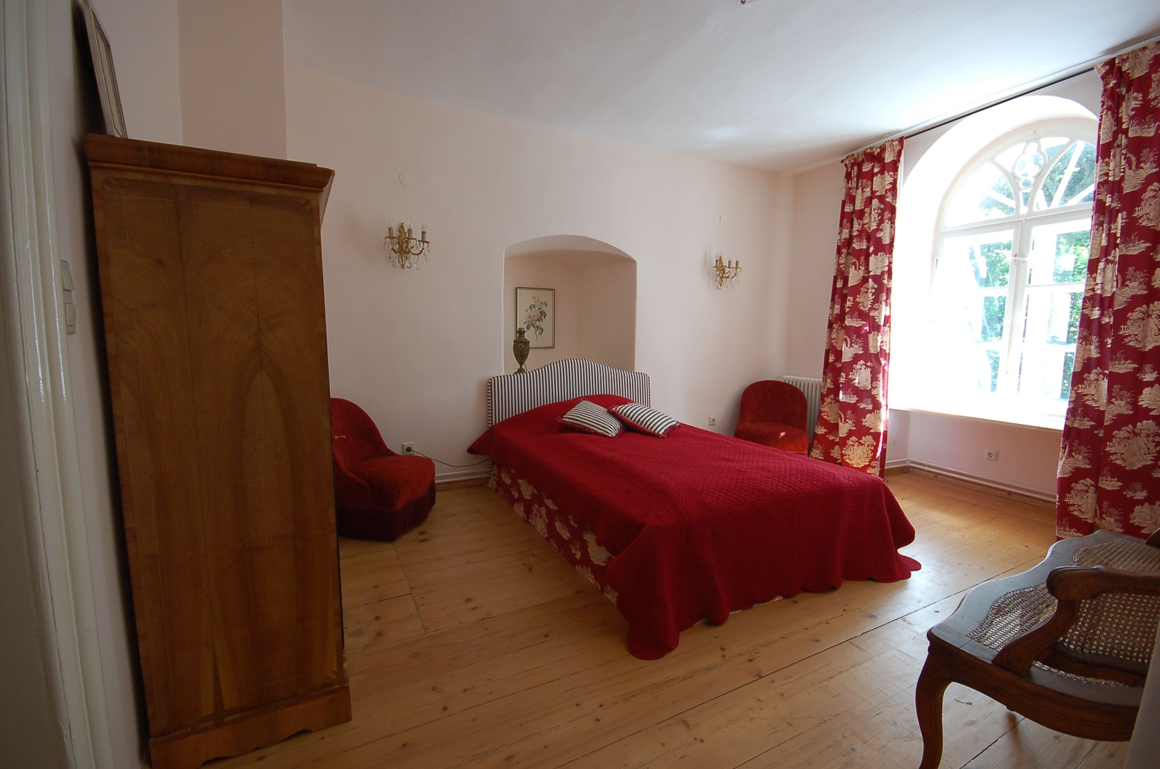 Hangulatos hálószoba piros ággyal, piros függönyökkel és fabútorokkal.