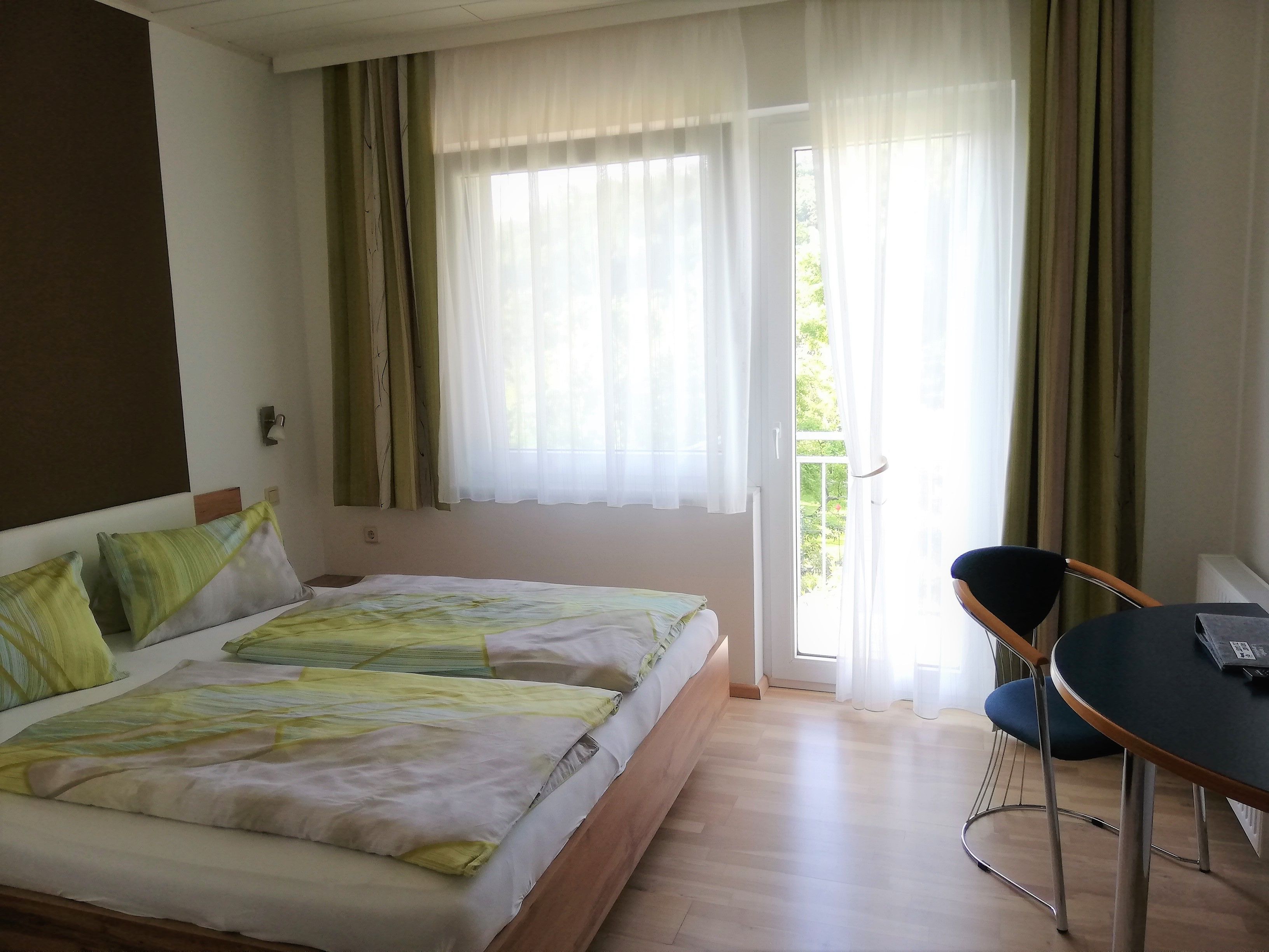 Kétágyas szoba egy ággyal, asztallal és székkel. Az erkély egy üvegajtón keresztül látható.