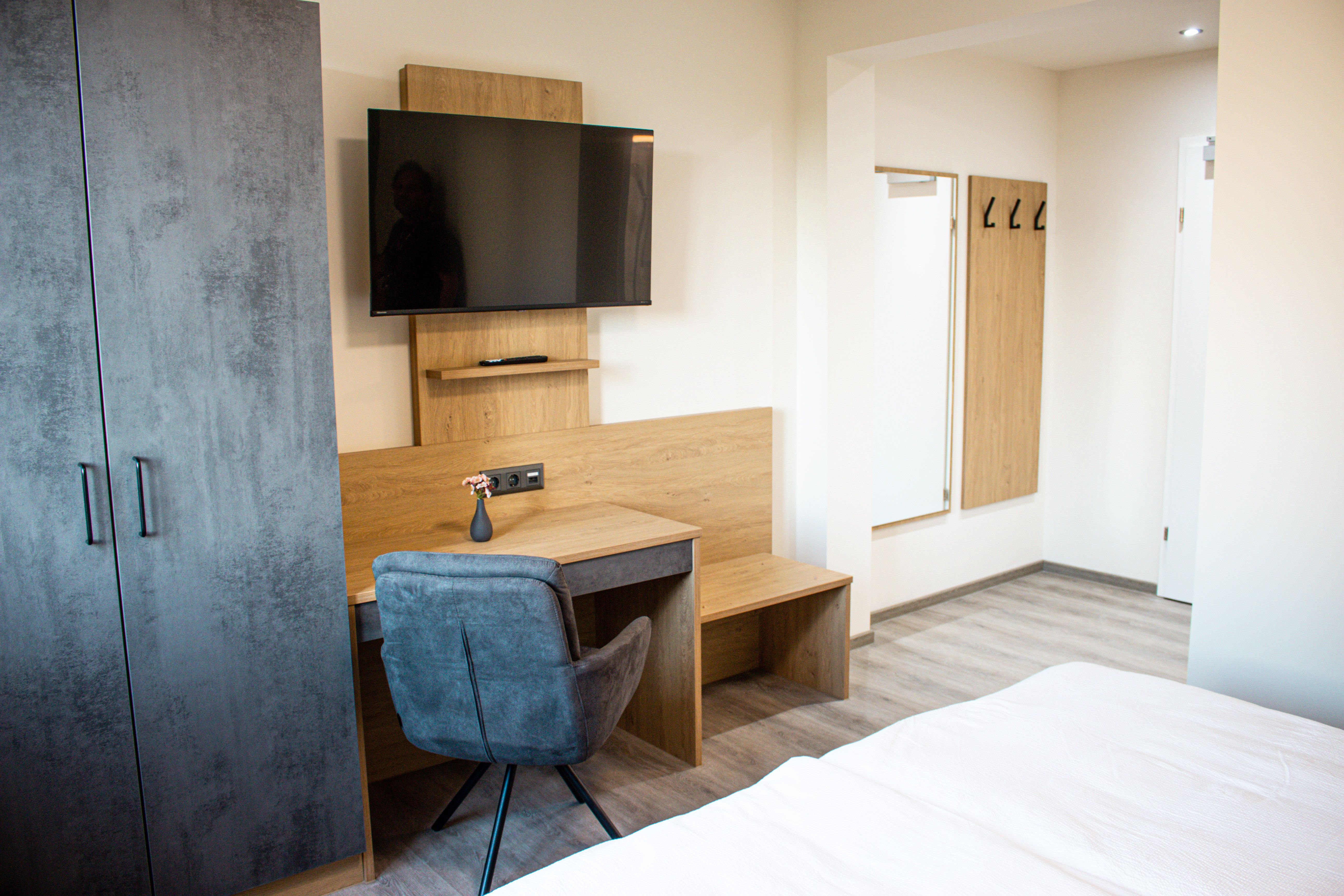 Modernül berendezett szállodai szoba íróasztallal, TV-vel, szekrénnyel és tükörrel.