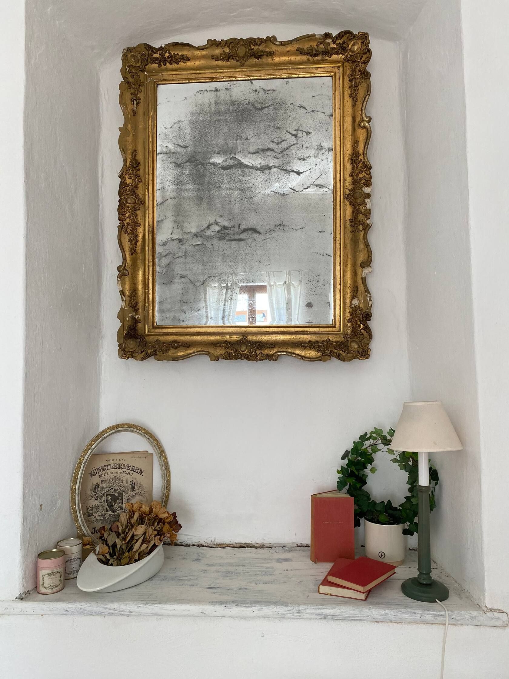 Antik tükör arany díszítéssel egy díszített ablakpárkány felett.