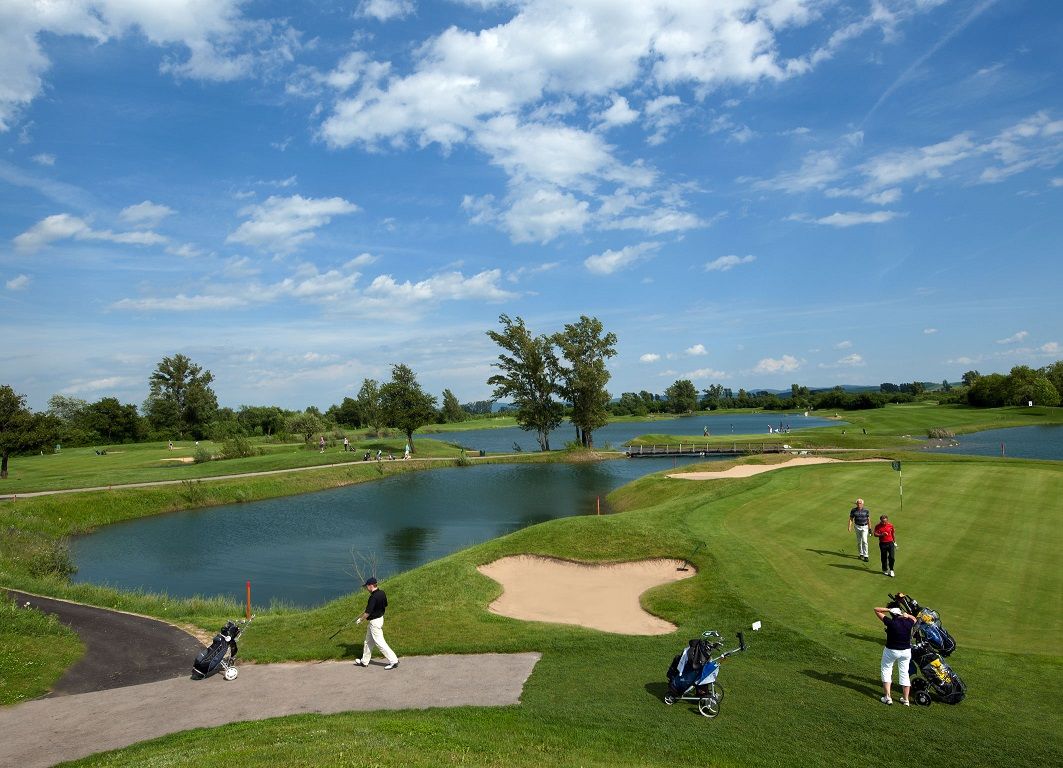 Golfpálya vízakadályokkal és játékosokkal a kék ég alatt.