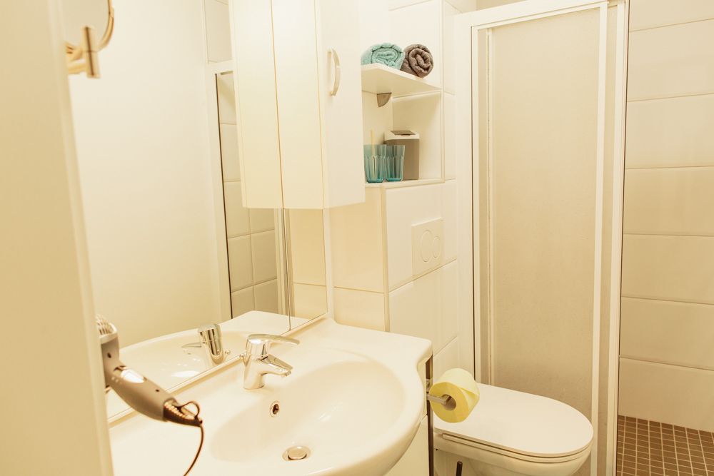 Kis fürdőszoba mosdóval, tükörrel, zuhanyzóval és WC-vel.