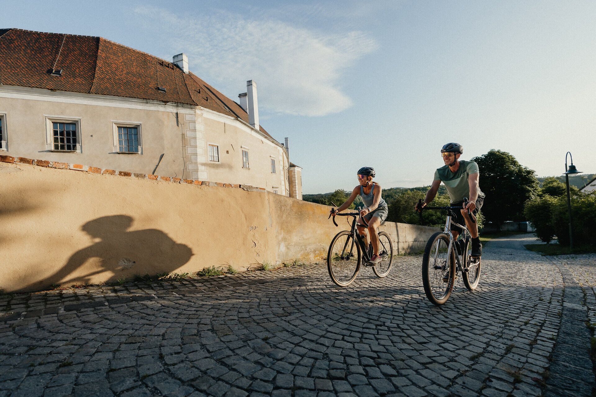 Két kerékpáros teker a macskaköves úton a régi városfal mentén Drosendorfban.