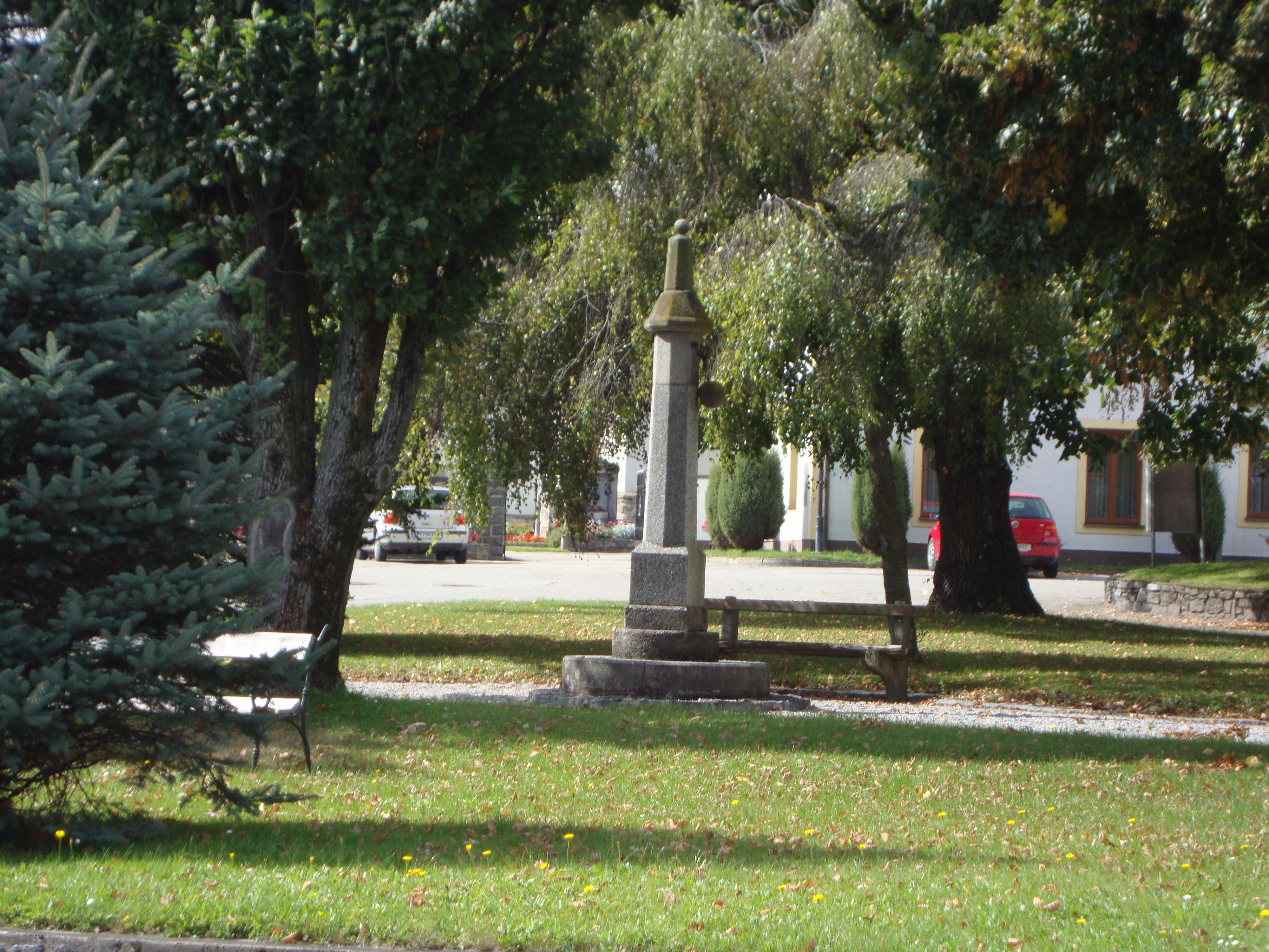Egy kis park egy kő emlékművel és egy fákkal körülvett paddal.