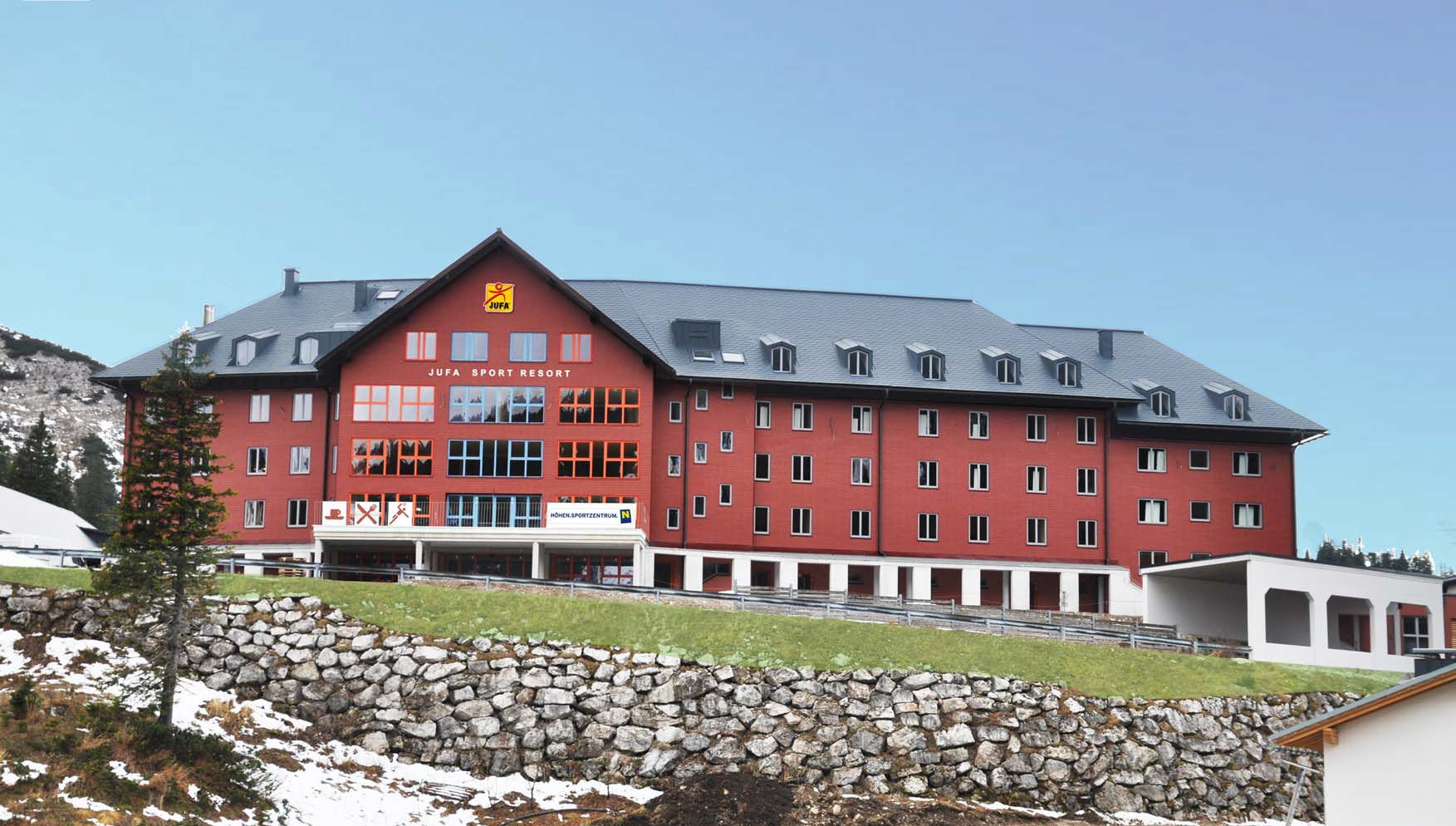 A Jufa Sport Resort nagy piros épülete egy hegyvidéki tájban.