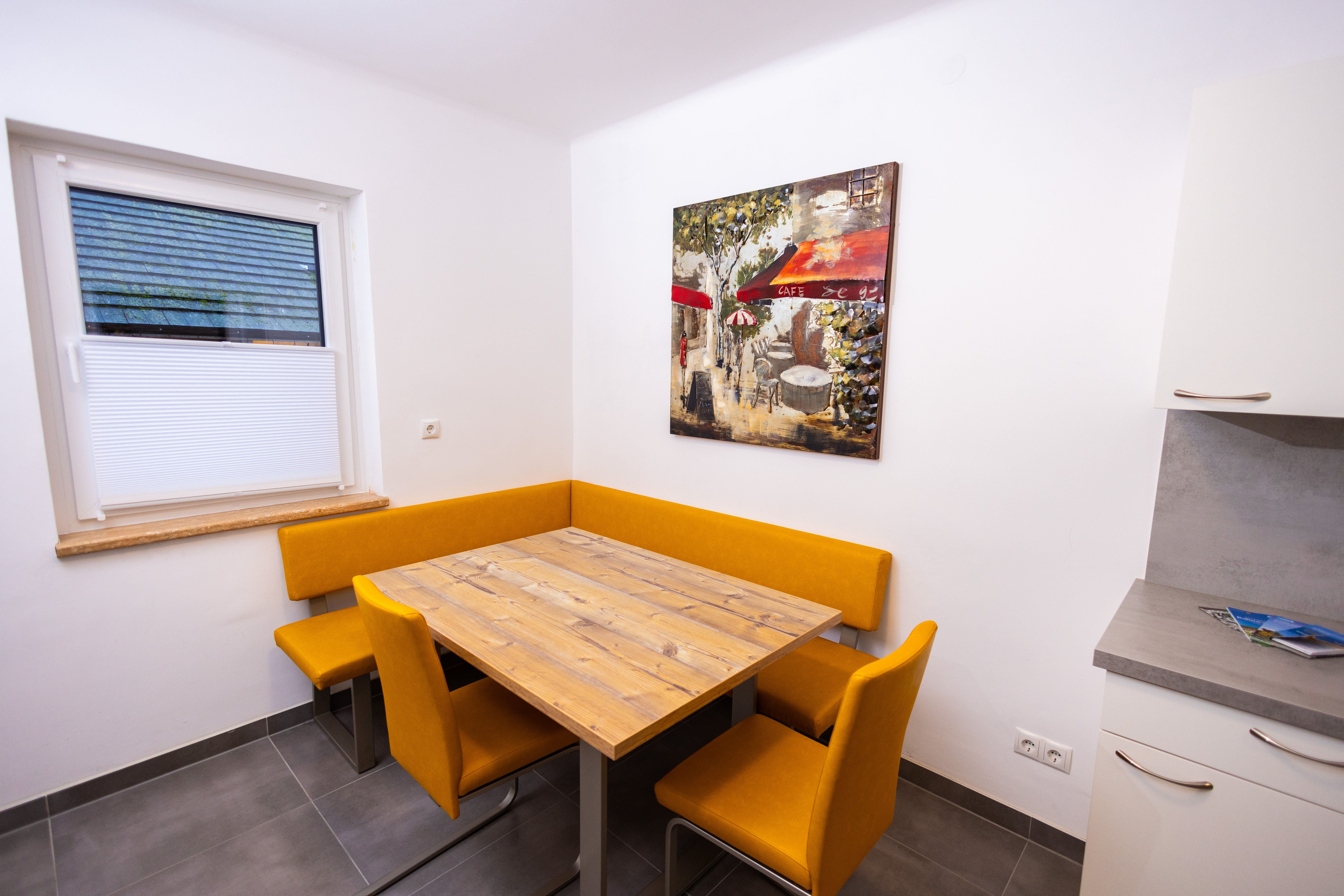 Étkezőhelyiség fa asztallal, sárga székekkel és egy kávézó falfestményével.