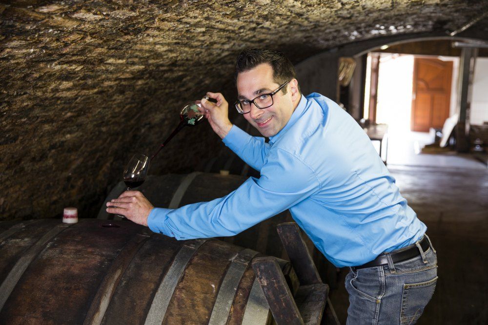 Kék inges férfi bort merít egy hordóból egy borospincében.