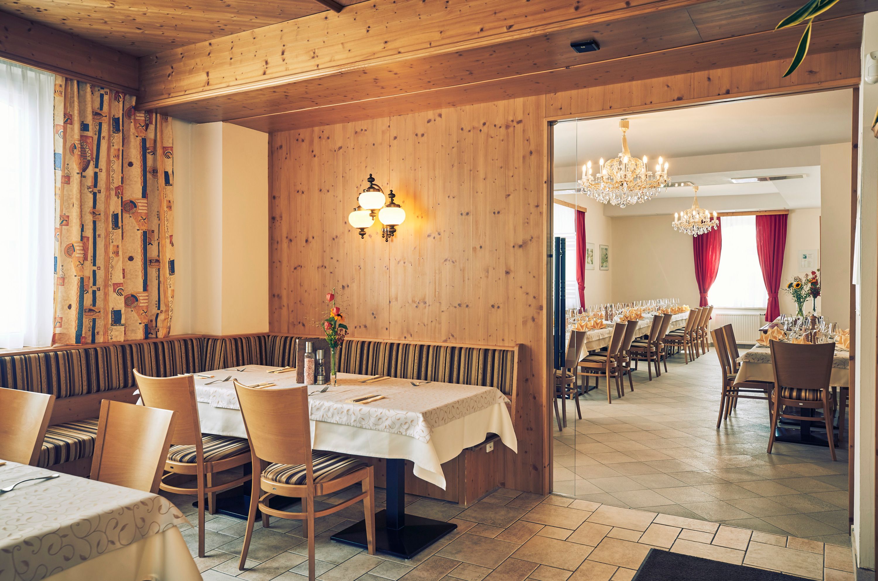 Hangulatos vendégszoba fából készült falakkal és egy szomszédos díszteremmel, csillárokkal és terített asztalokkal.