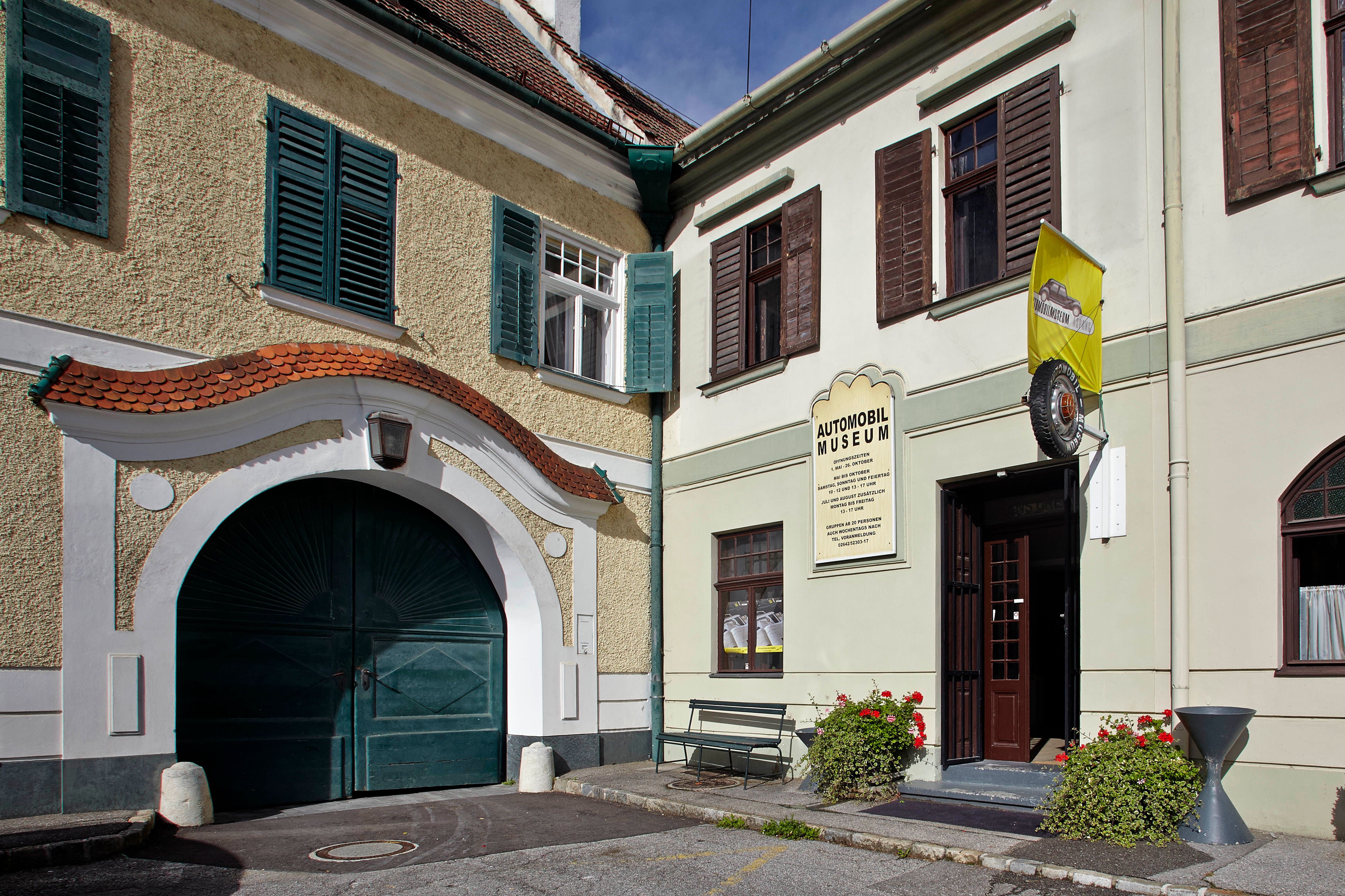 Az Aspang Market Autómúzeum bejárata sárga zászlóval és virágokkal.