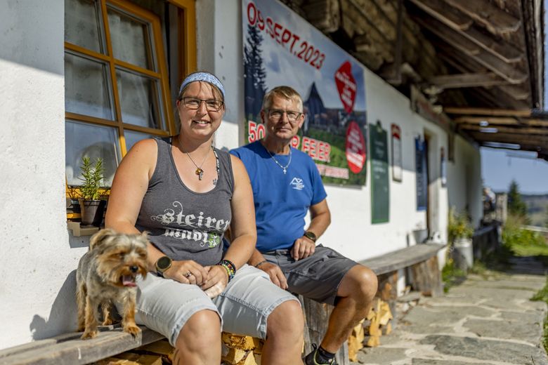 Két ember ül egy épület előtt egy kutyával, a háttérben egy plakát a 2023. szeptember 09-i dátummal.