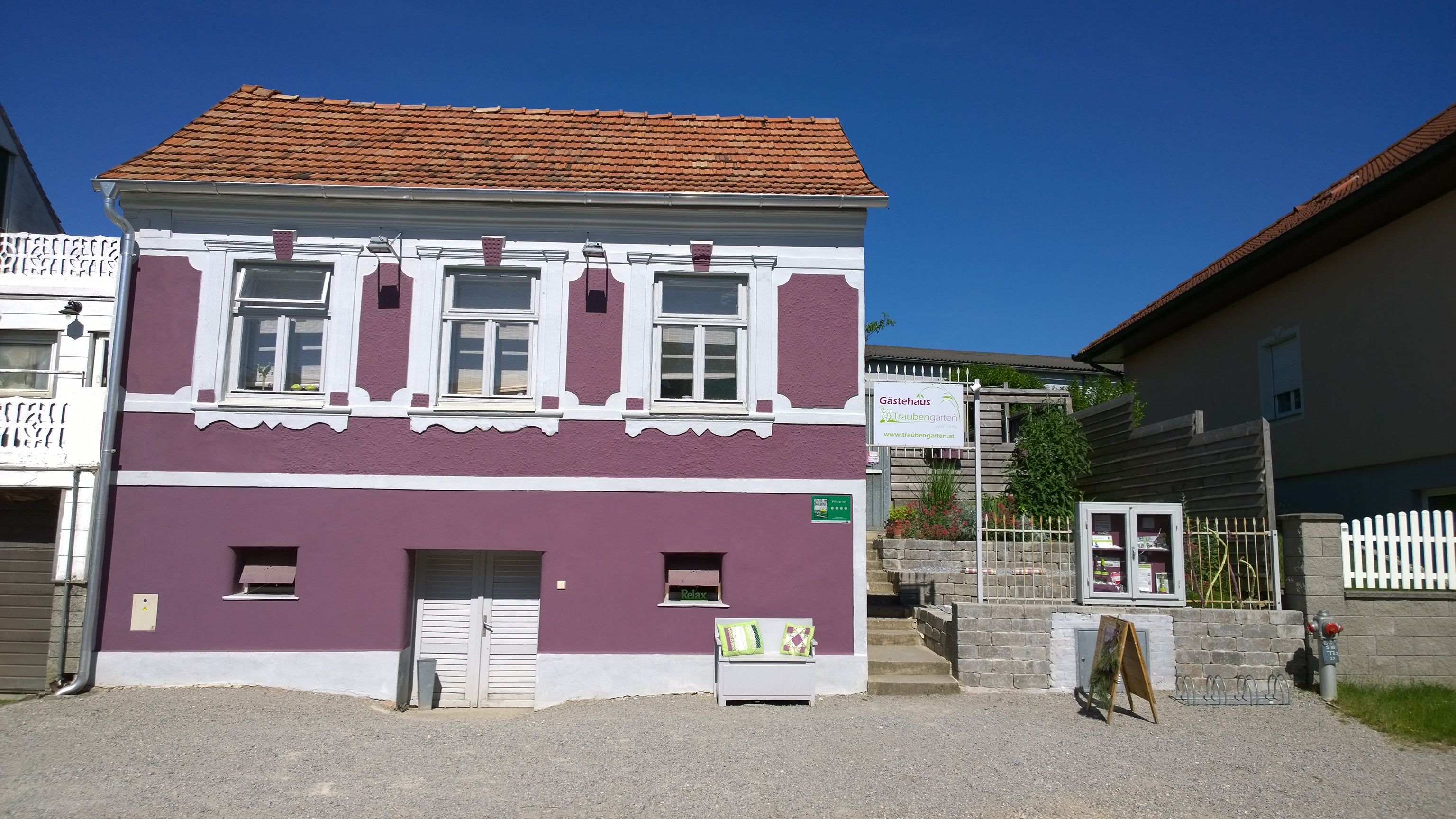 Egy lila ház külső nézete fehér ablakkeretekkel és egy vendégház felirattal.