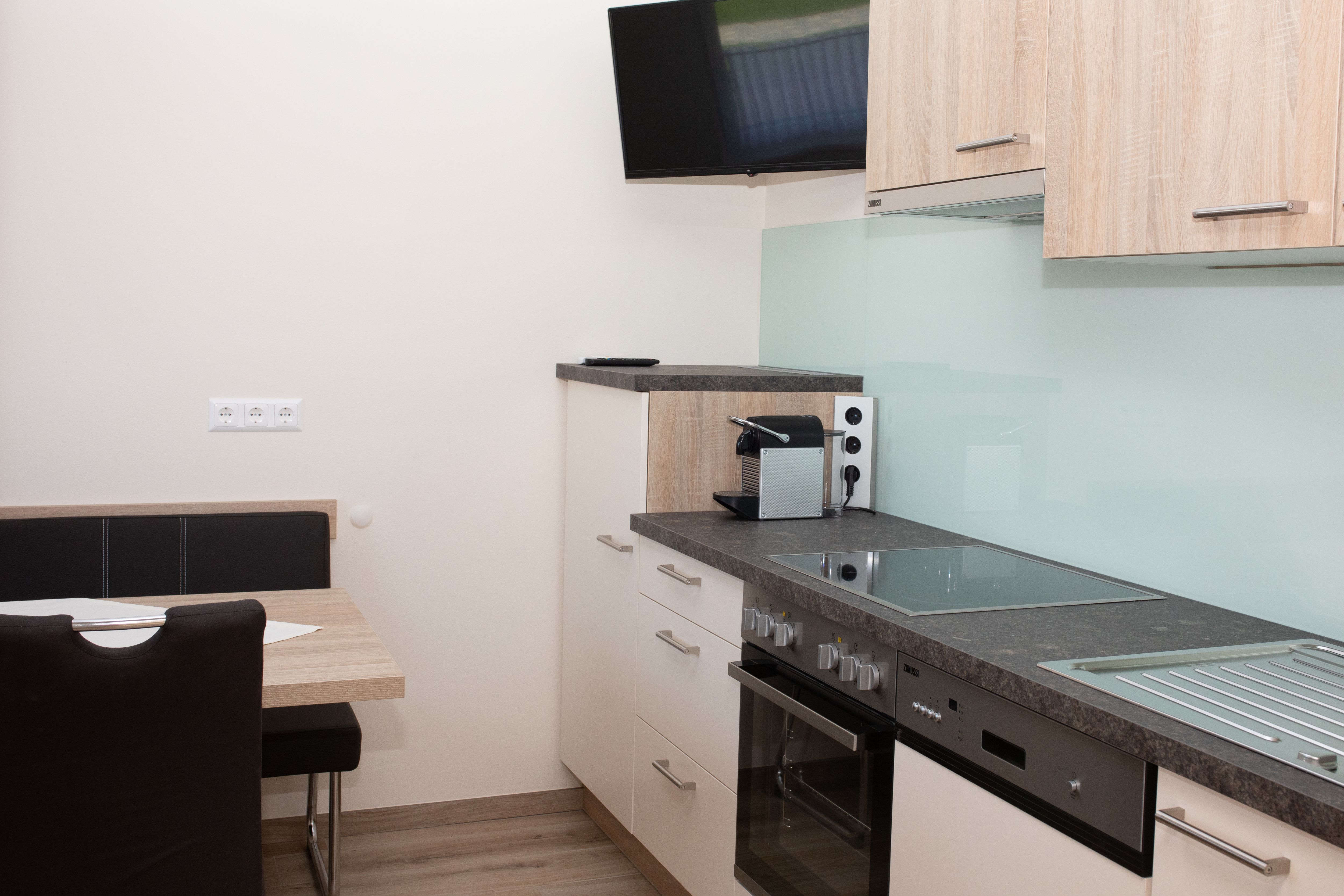 Modern konyha, tűzhely, mosogató, kávéfőző és fali TV.