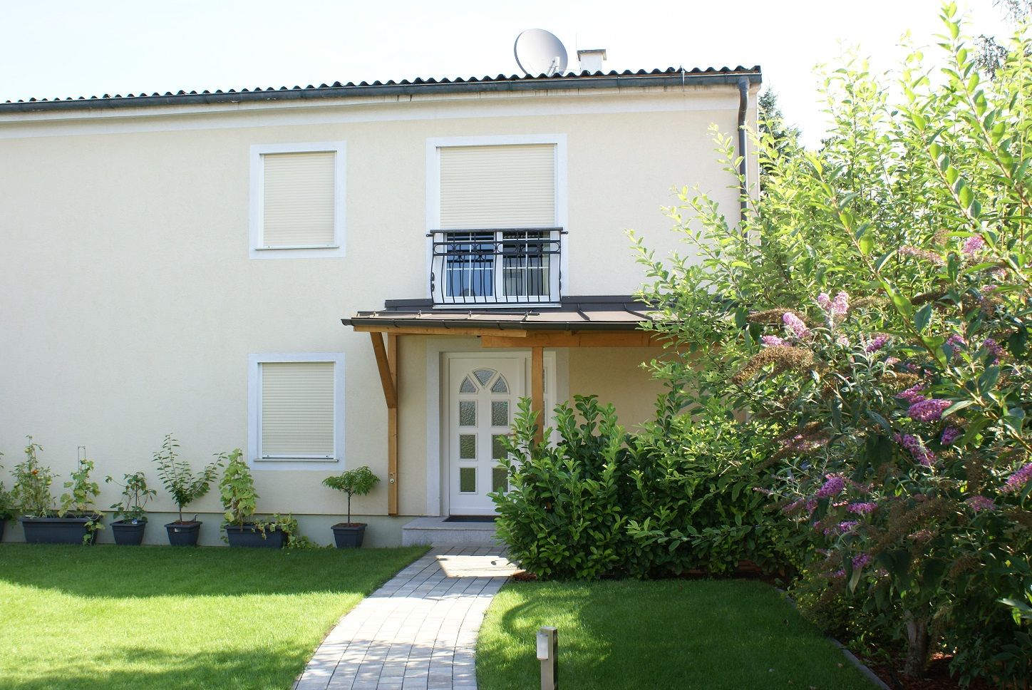 Egy kétszintes ház külső nézete kerttel és növényekkel.