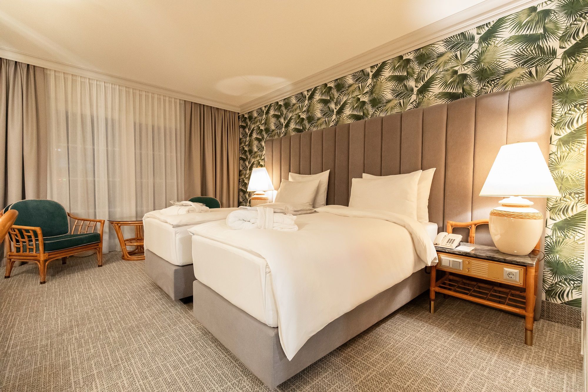 Hotelszoba két egyszemélyes ággyal, trópusi tapétával és éjjeli lámpákkal.