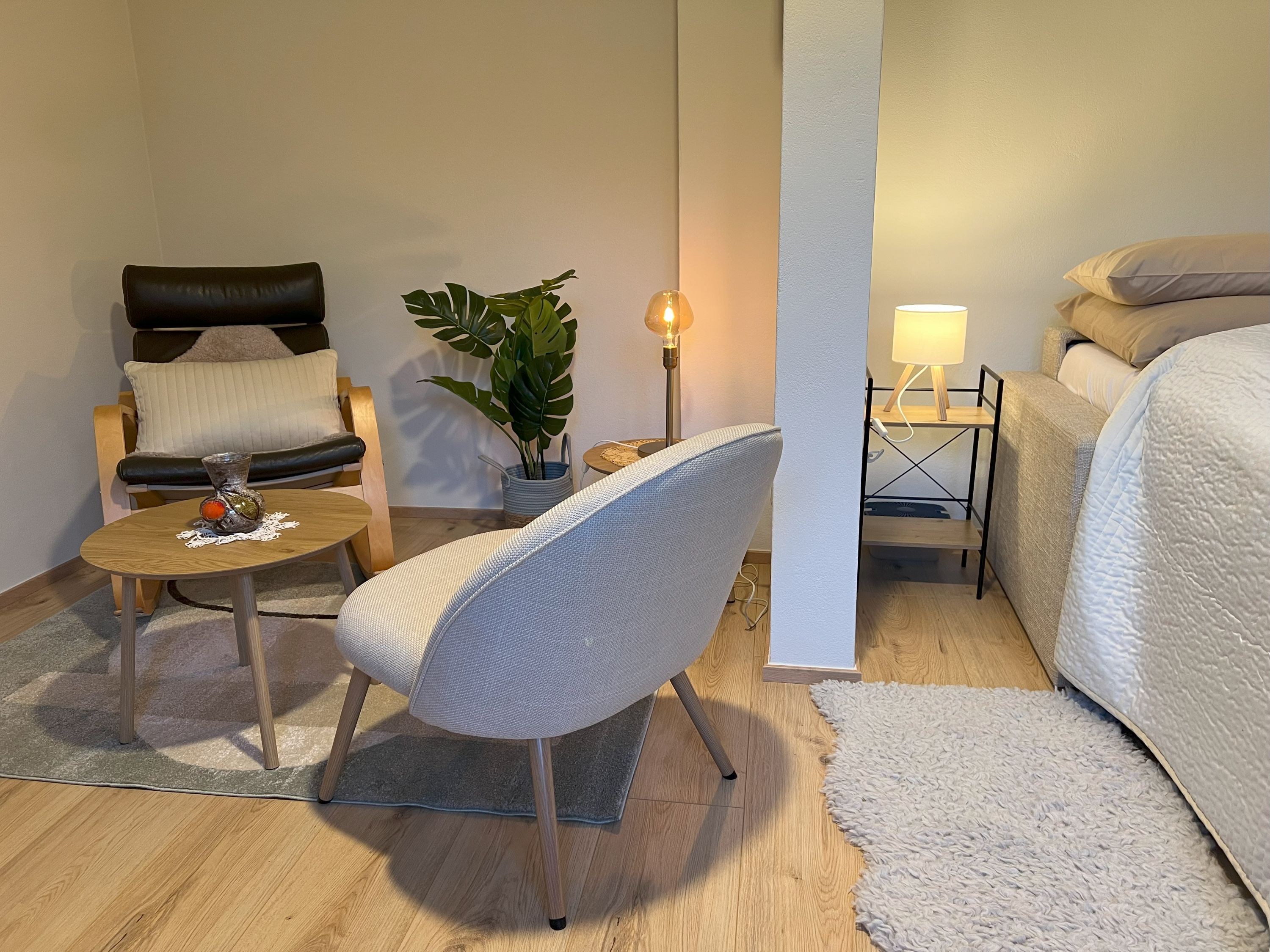 Hangulatos hálószoba fotel, asztal, növény és ágy.