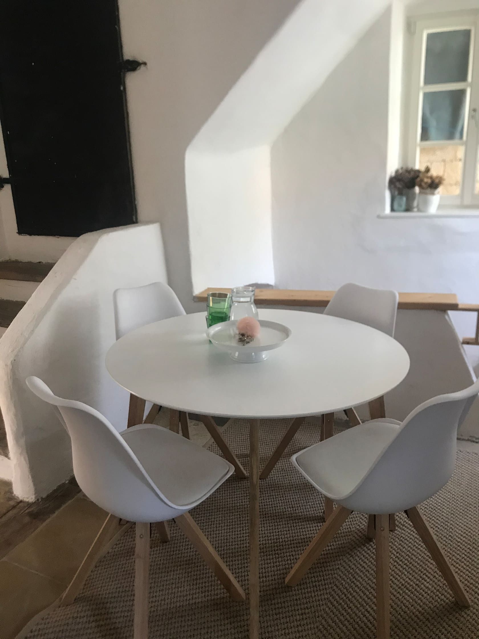 Modern ülősarok kerek asztallal és négy fehér székkel egy világos szobában.