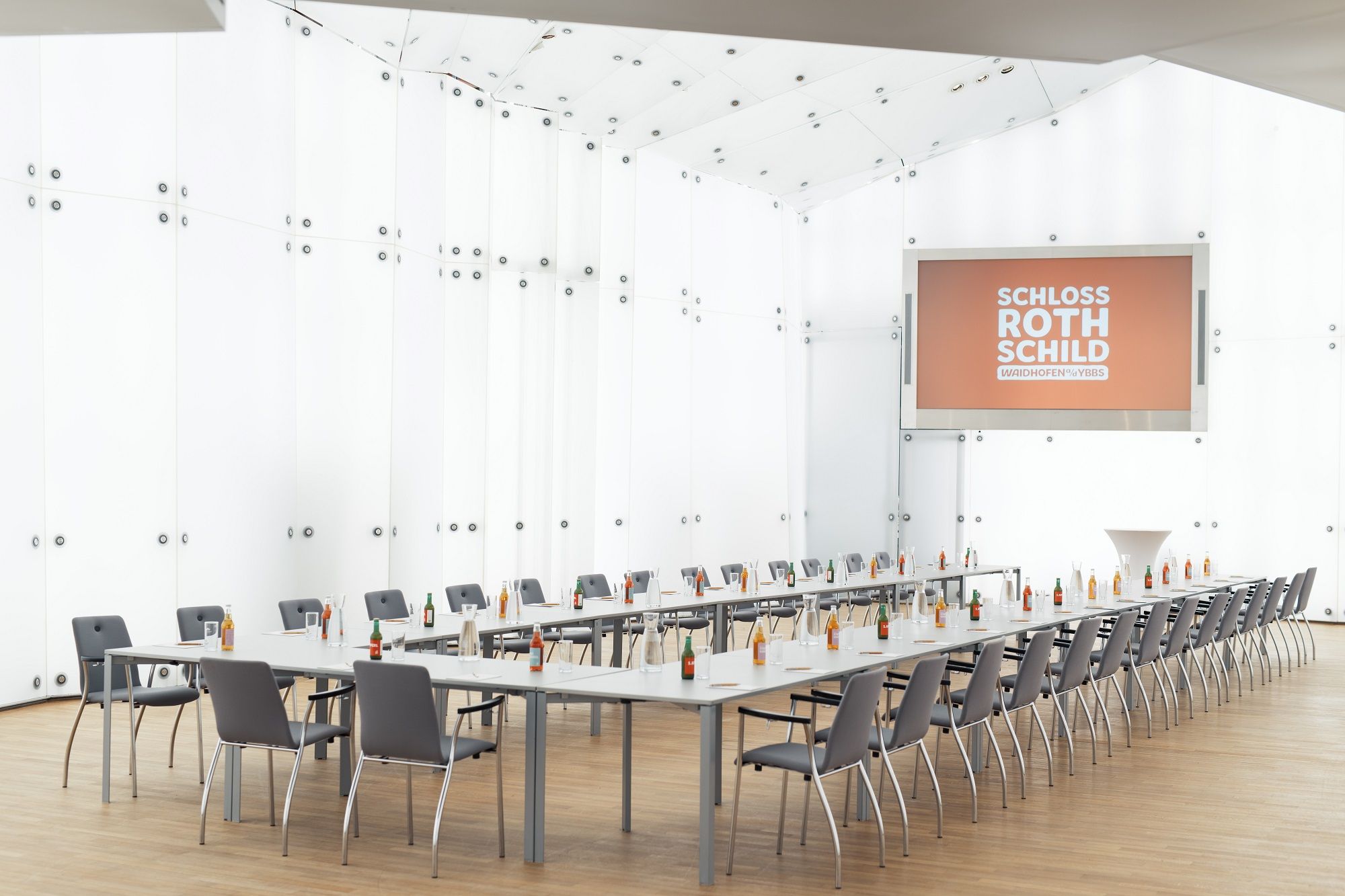 Modern konferenciaterem a Rothschild-kastélyban, hosszú asztalokkal, székekkel és italokkal.