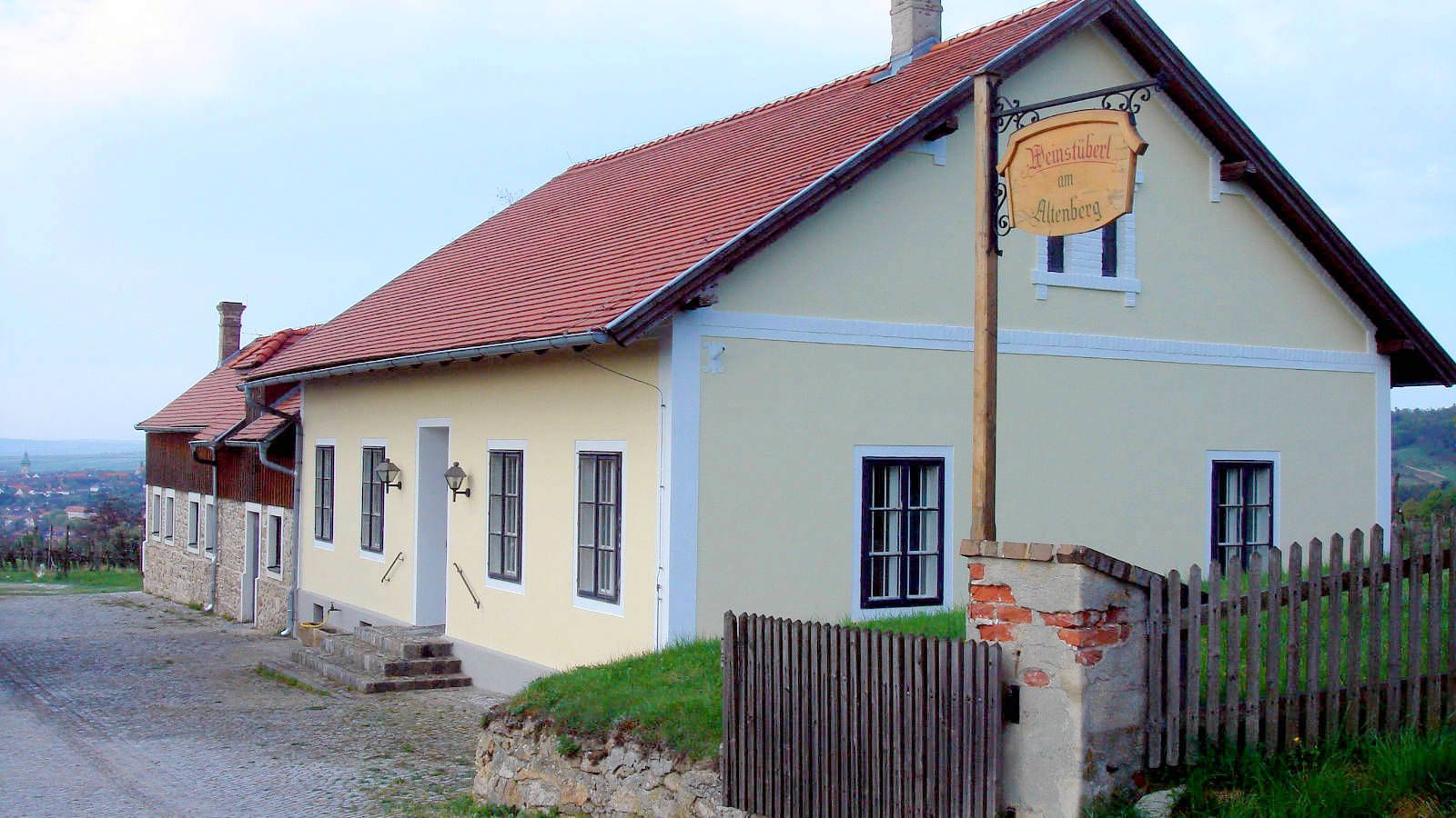 Borászház sárga homlokzattal és piros tetővel vidéki környezetben.