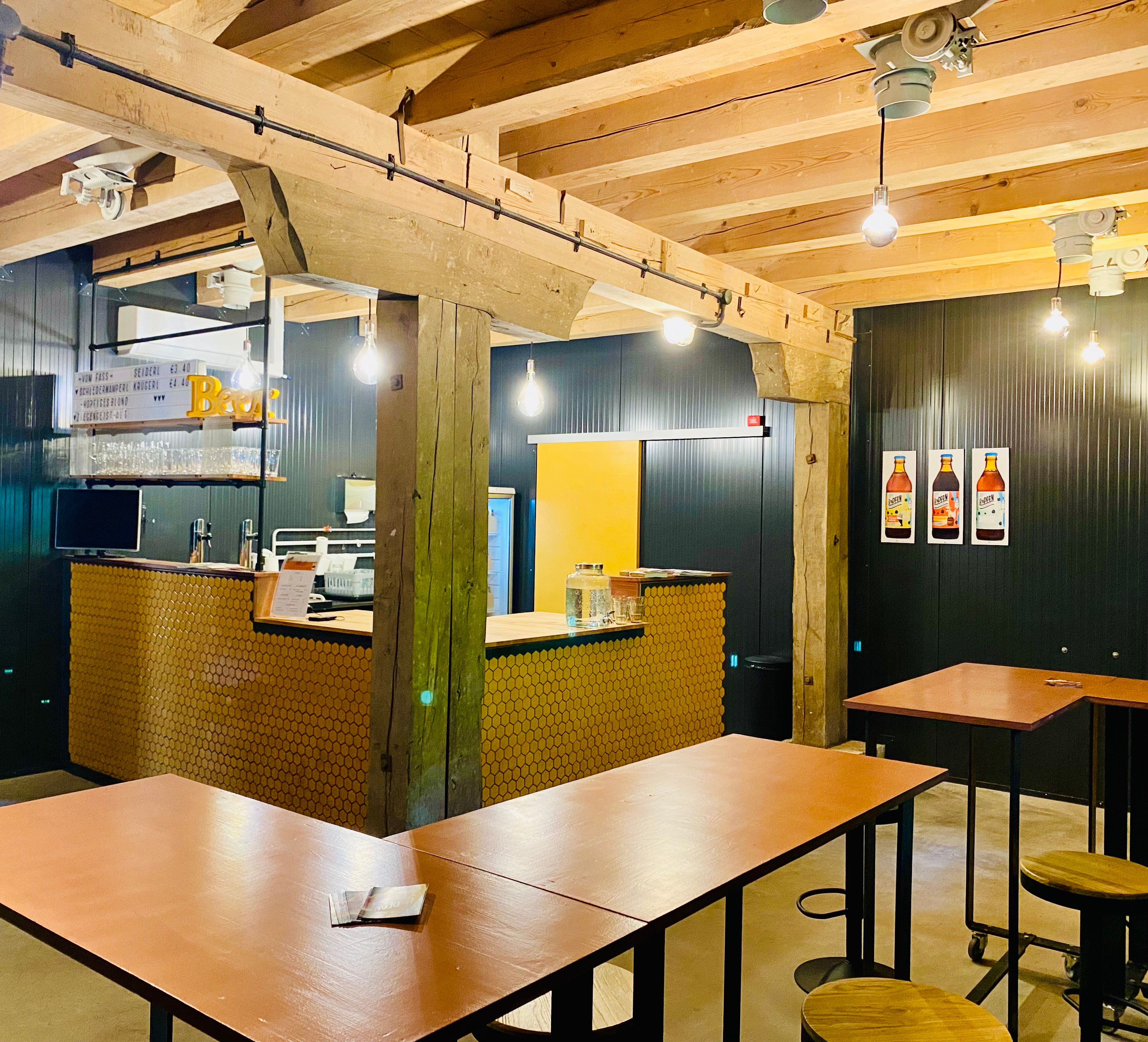 Egy modern kávézó belső nézete, fagerendákkal, bárpultokkal és magas asztalokkal.