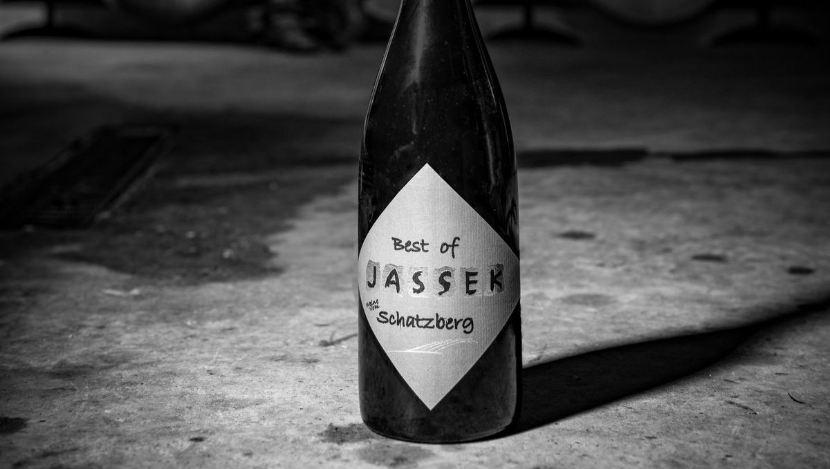 Fekete-fehér fotó egy borosüvegről "Best of Jassek Schatzberg" felirattal a betonpadlón.