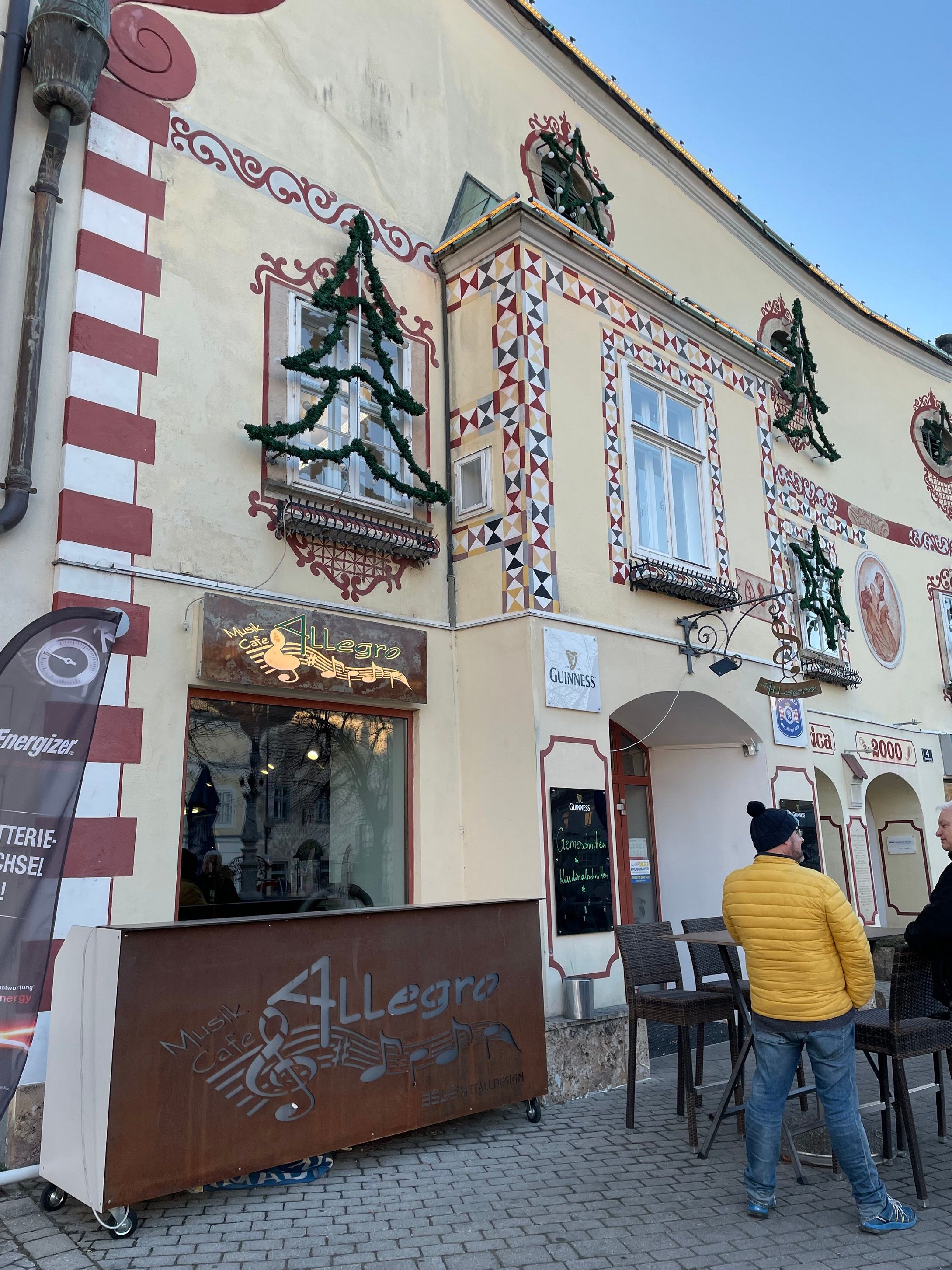 A Cafe Allegro külső nézete díszített homlokzattal és két beszélgető emberrel.