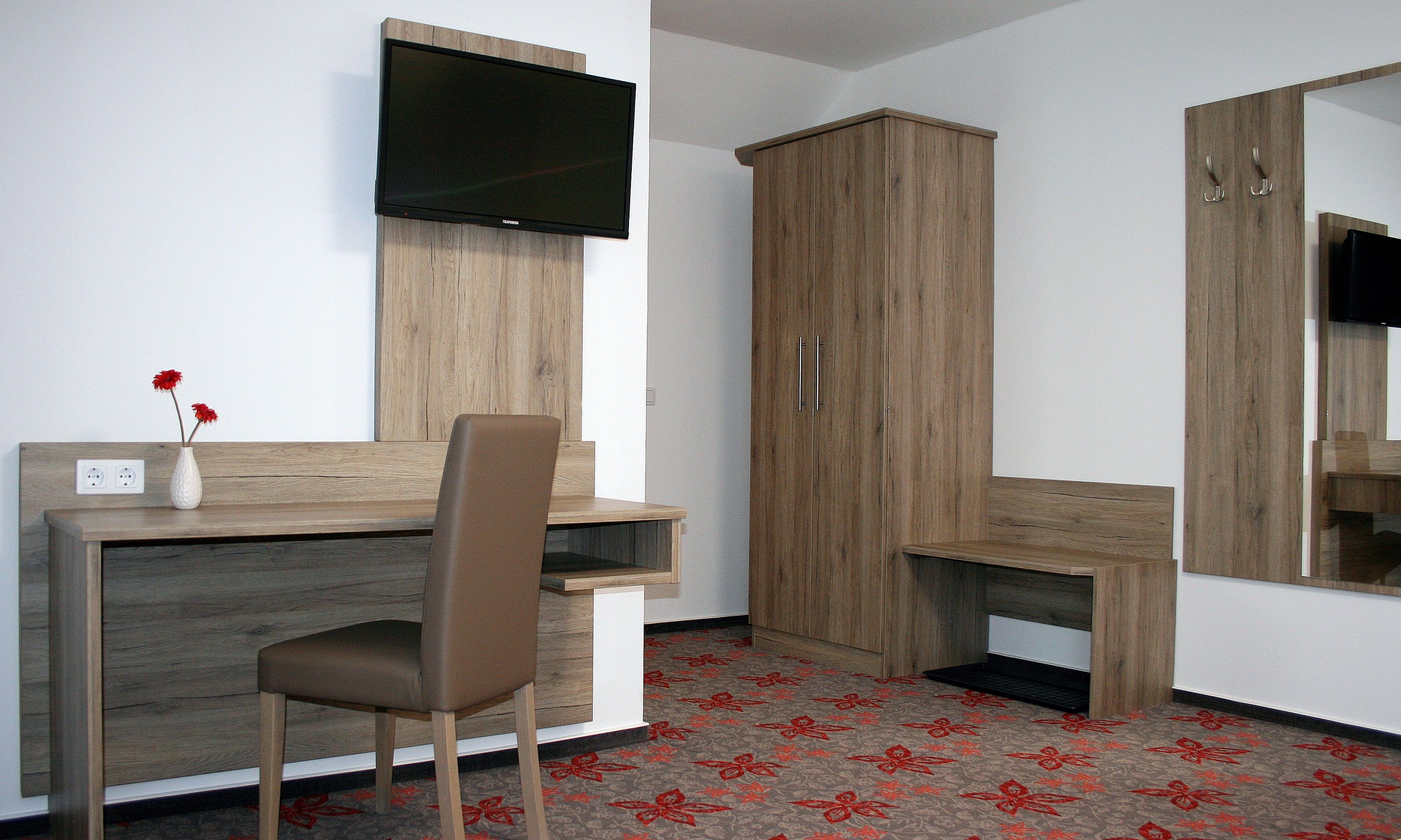 Hotelszoba íróasztallal, székkel, televízióval és szekrénnyel.