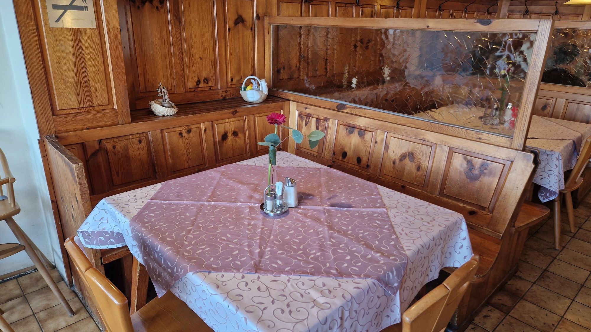 Hangulatos asztal egy rusztikus vendégszobában, faburkolattal, terítővel és virágos vázával.