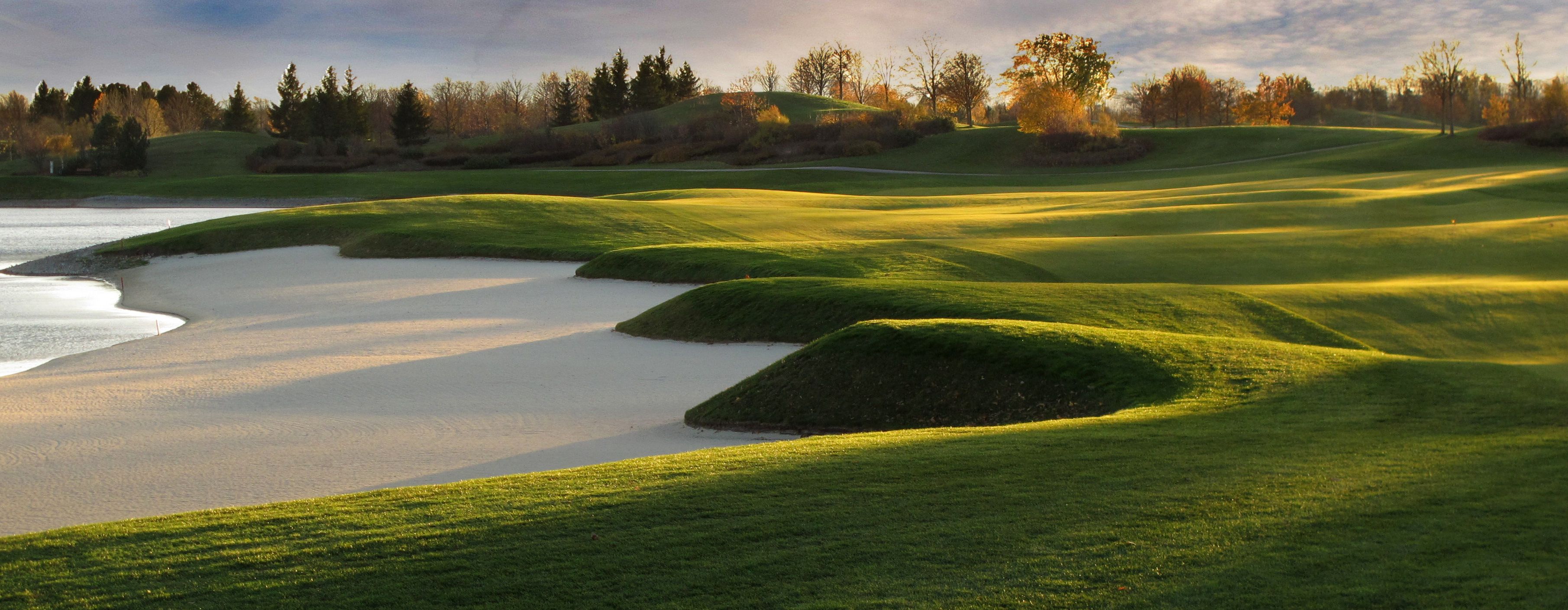 Panoráma egy golfpályáról homokbunkerekkel és zöld dombokkal a napfényben.