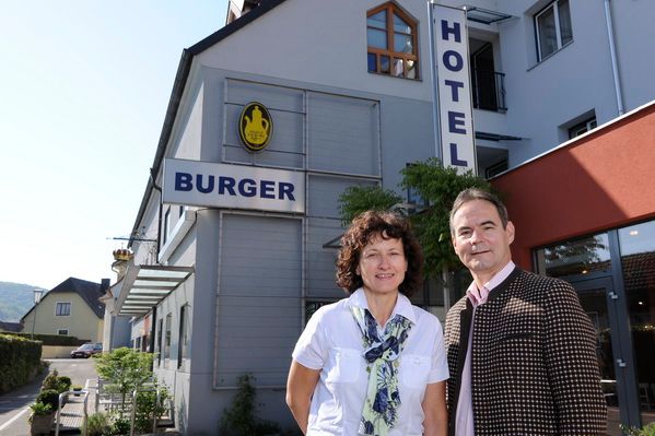 Egy férfi és egy nő áll a "Hotel Burger" feliratú épület előtt.