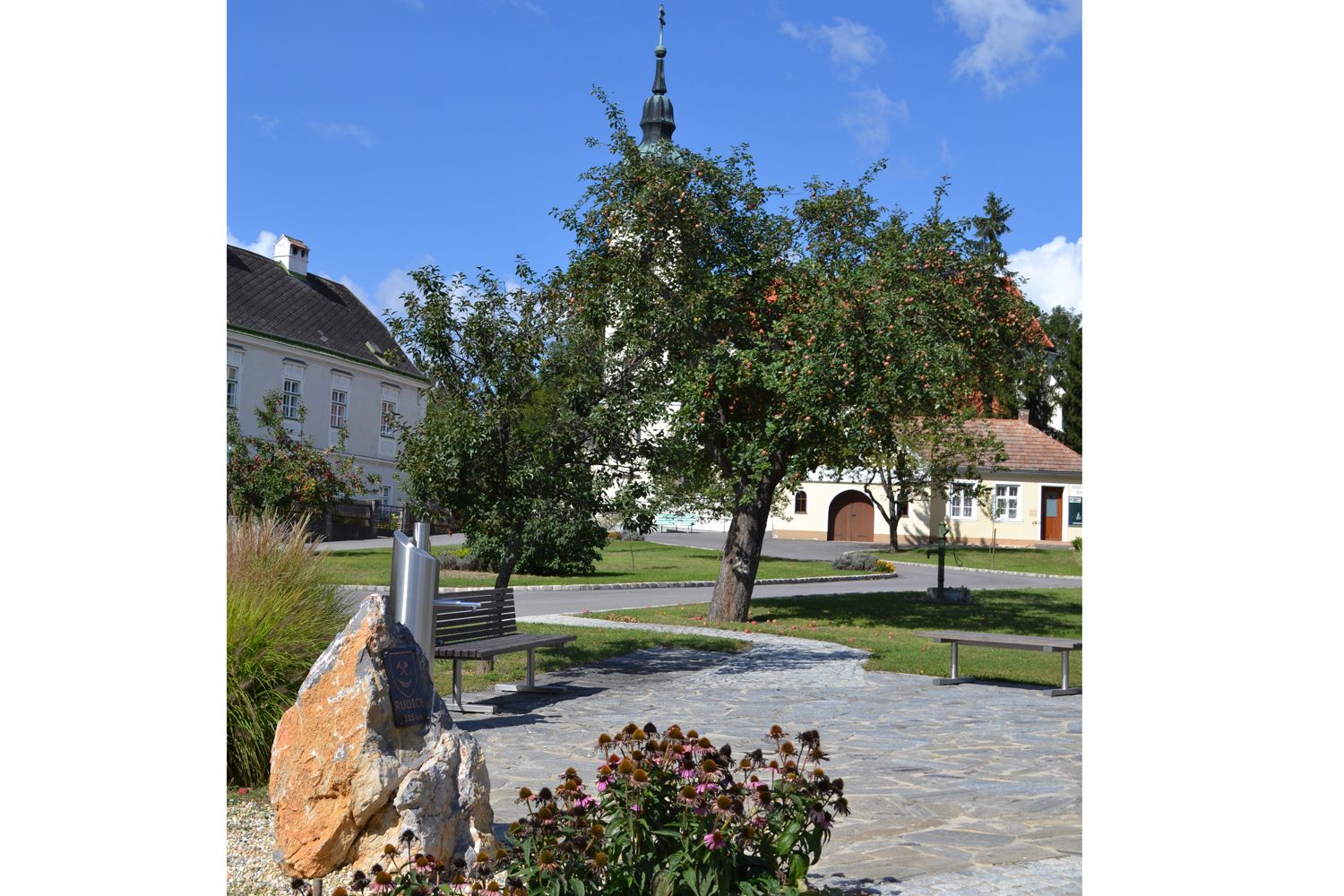 Hagenbergi főtér templommal, fákkal és padokkal.