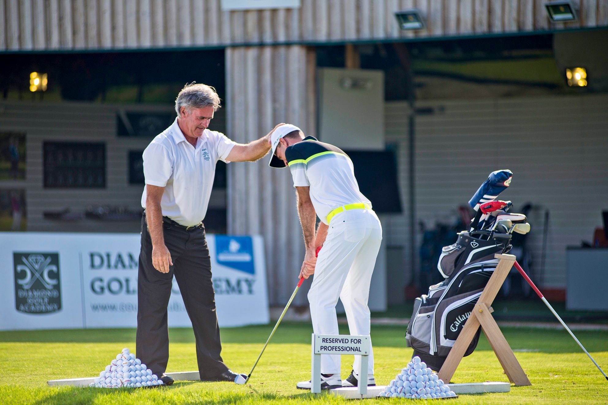 Egy golfoktató utasításokat ad egy tanítványnak a Diamond Golf Academy egyik gyakorló pályáján.