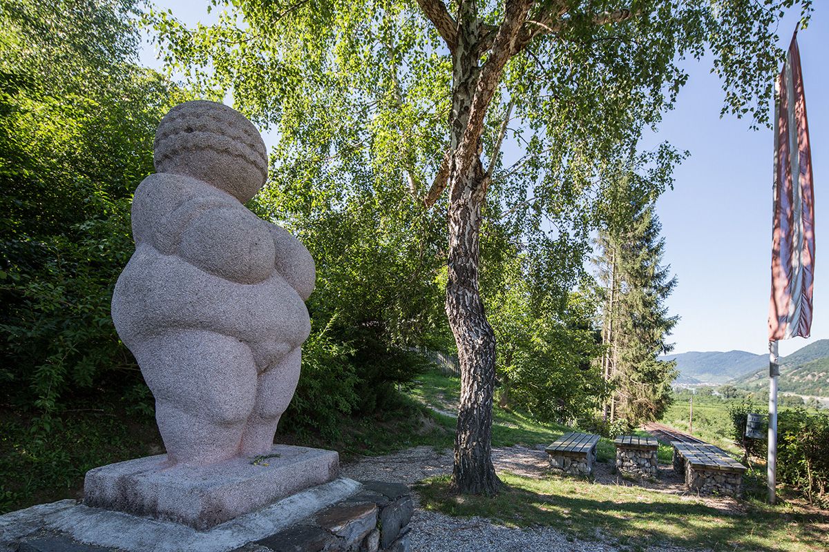 Vénusz egy talapzaton a háttérben fa és padok