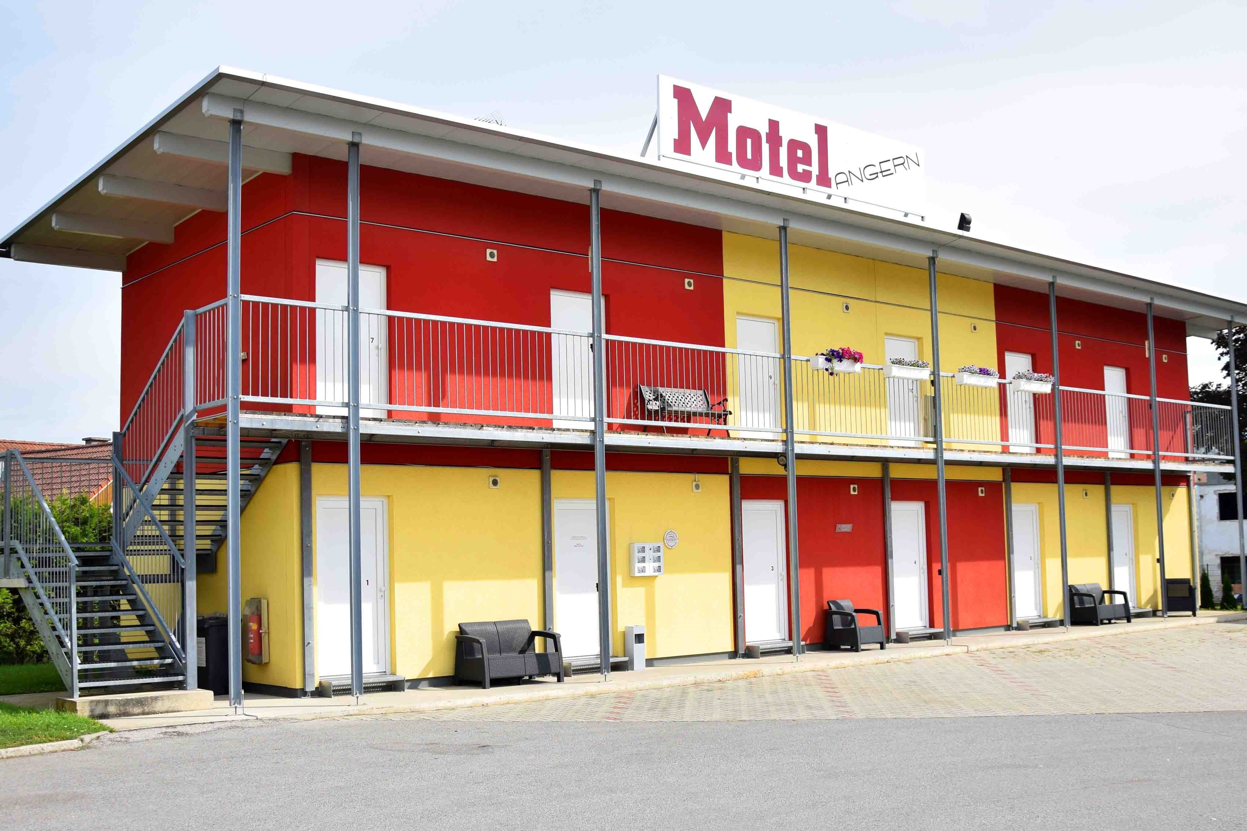 Kétemeletes motelépület sárga és piros falakkal, lépcsővel és erkéllyel.