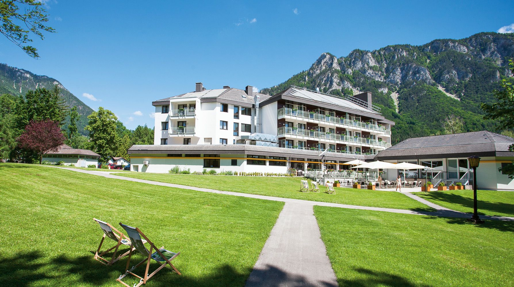 Parkhotel Hirschwang a hegyek hátterében, zöld pázsittal és nyugágyakkal.