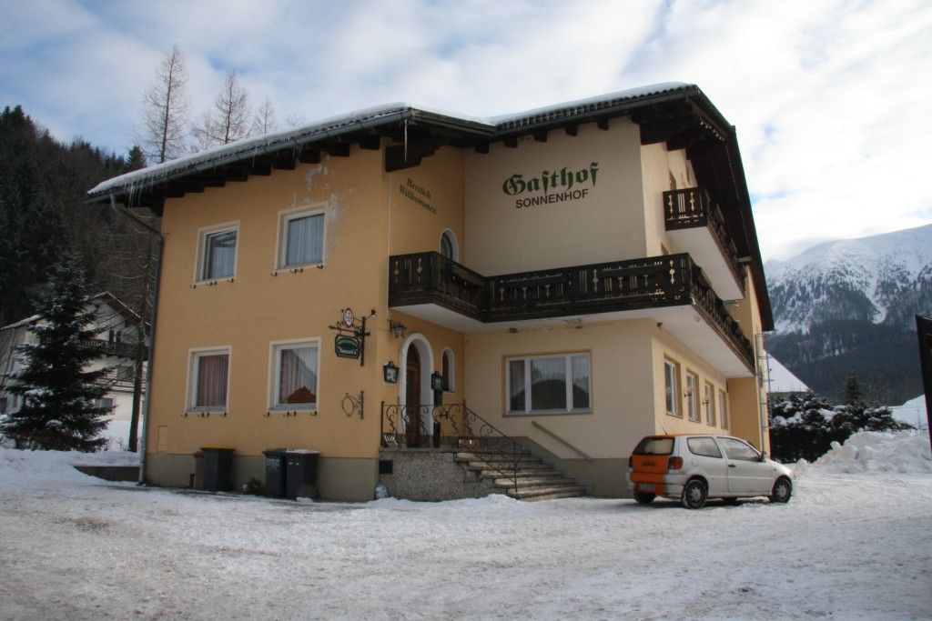 A "Gasthof Sonnenhof" feliratú sárga épület a hóban, hegyekkel körülvéve.
