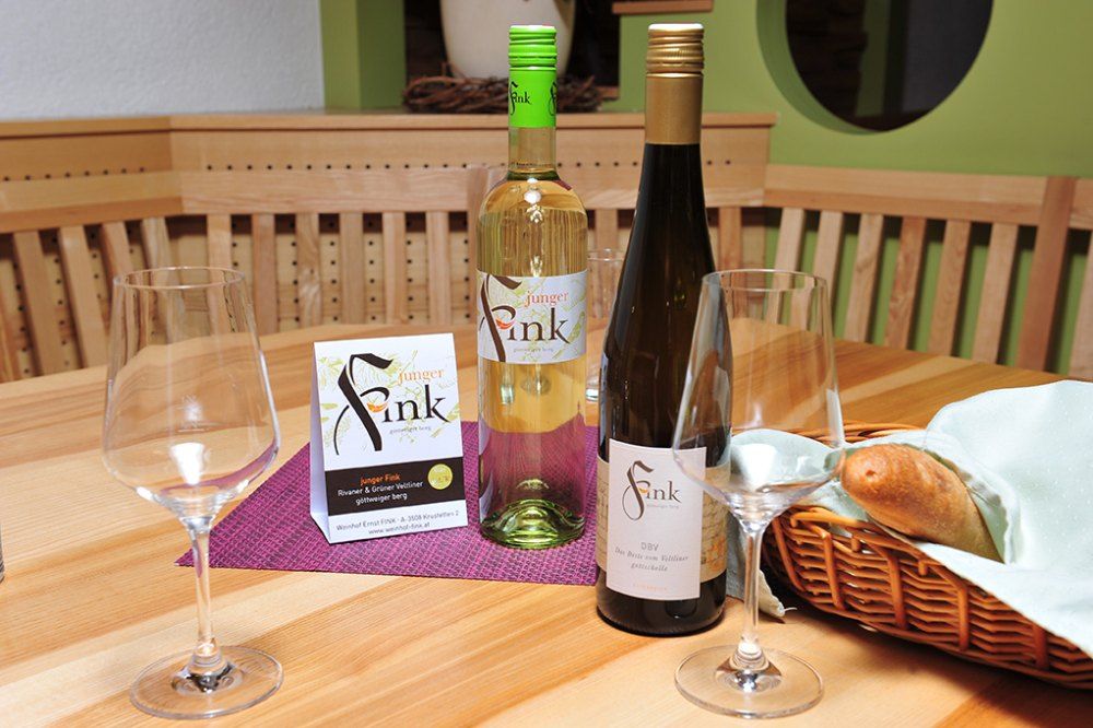 Két üveg bor és poharak egy faasztalon, kenyérkosárral.