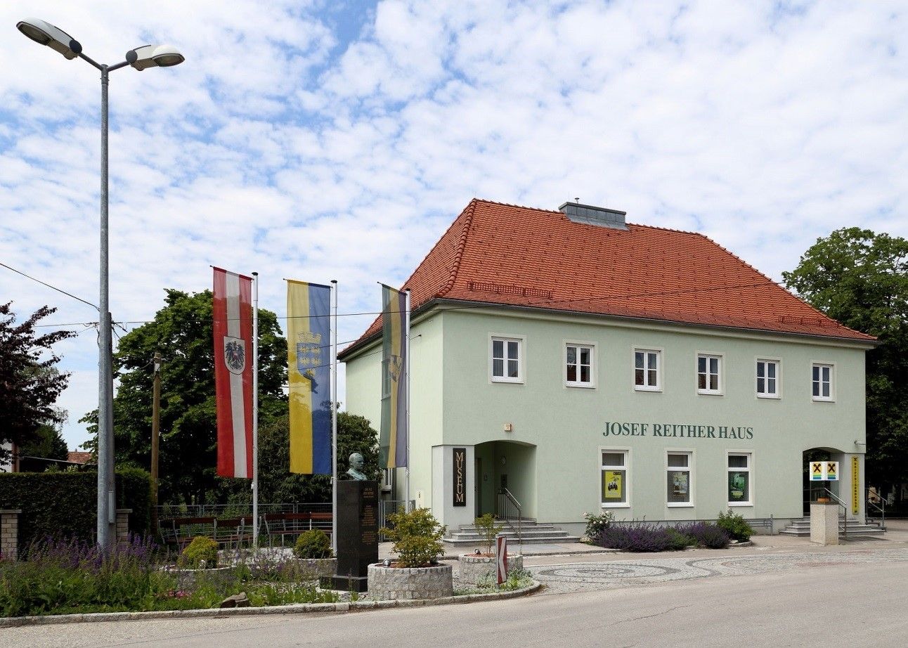 Josef Reither háza zászlókkal és mellszoborral az előtérben.