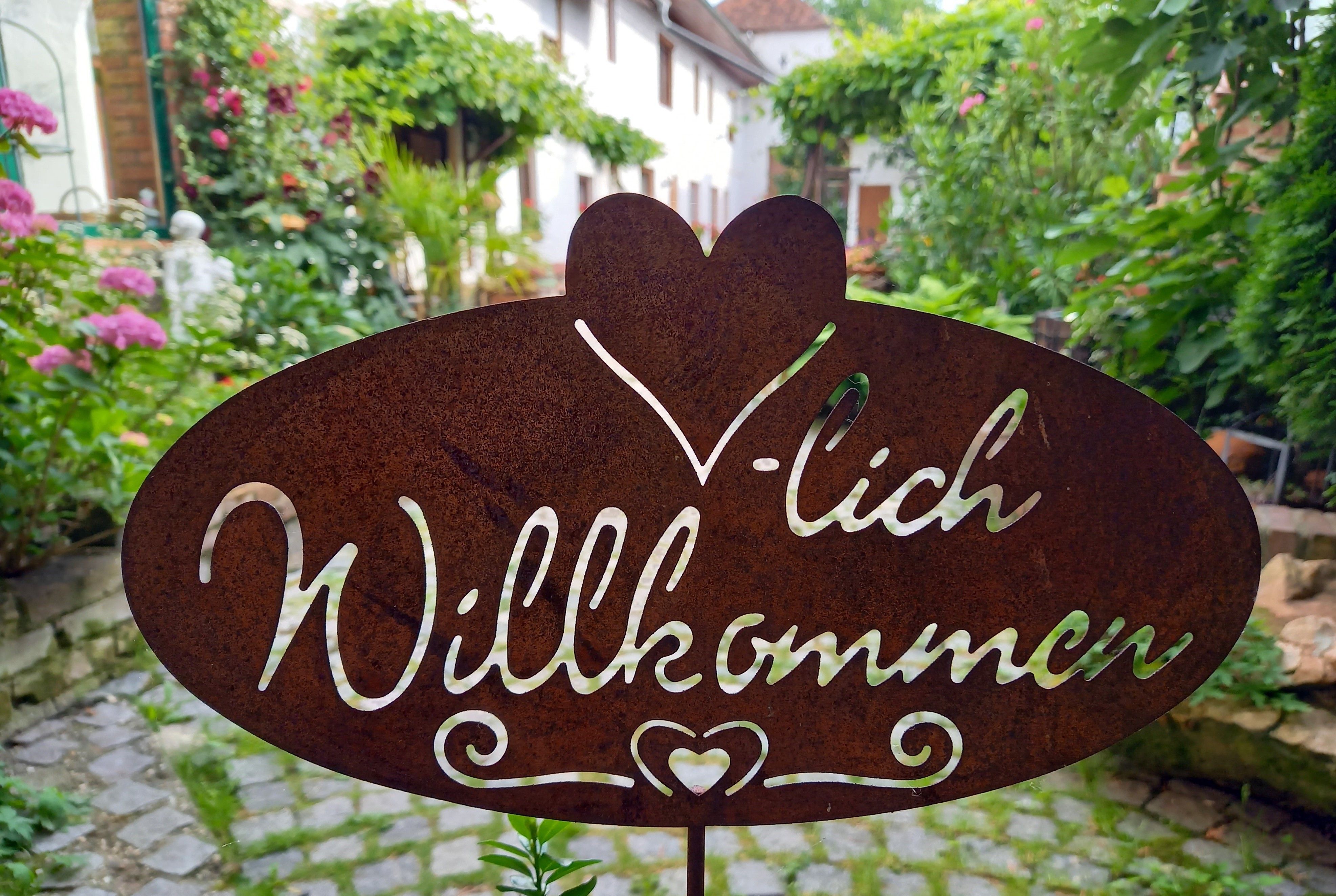 Fémtábla "Welcome" felirattal egy kertben.